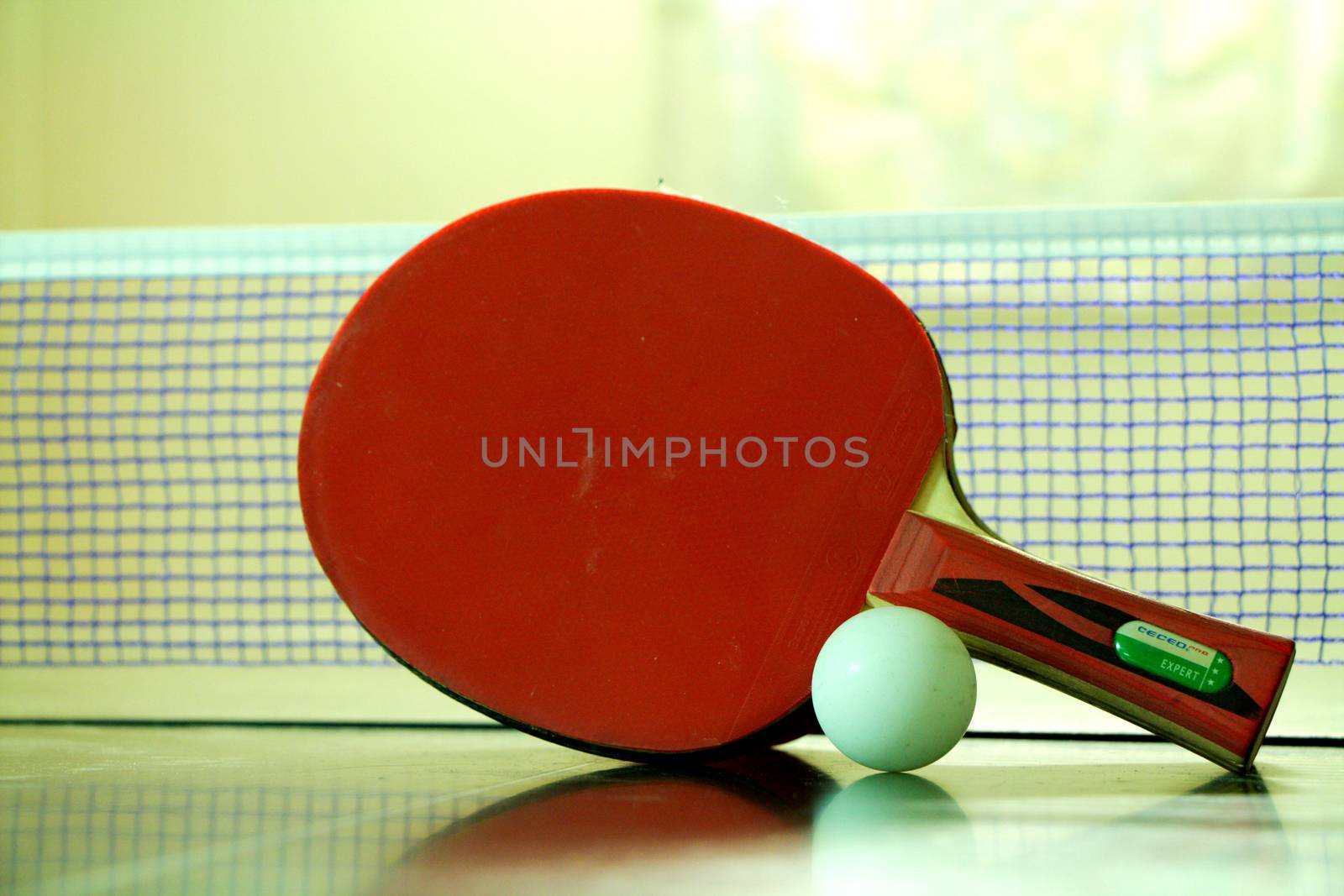 Two red table tennis or ping pong rackets and ball on a green table with blue net