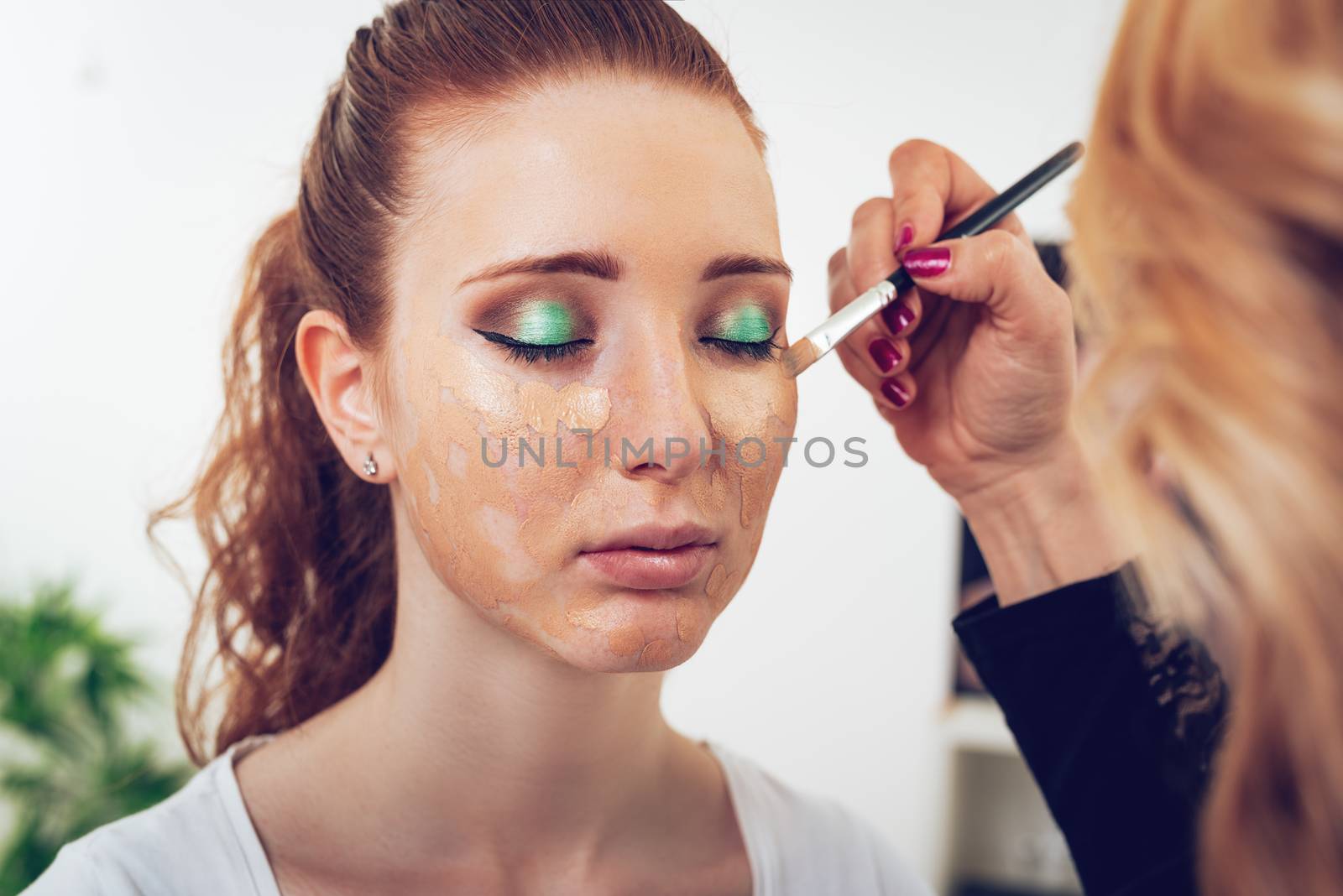 Makeup artist applying powder on a beautiful young woman's face. Close up.