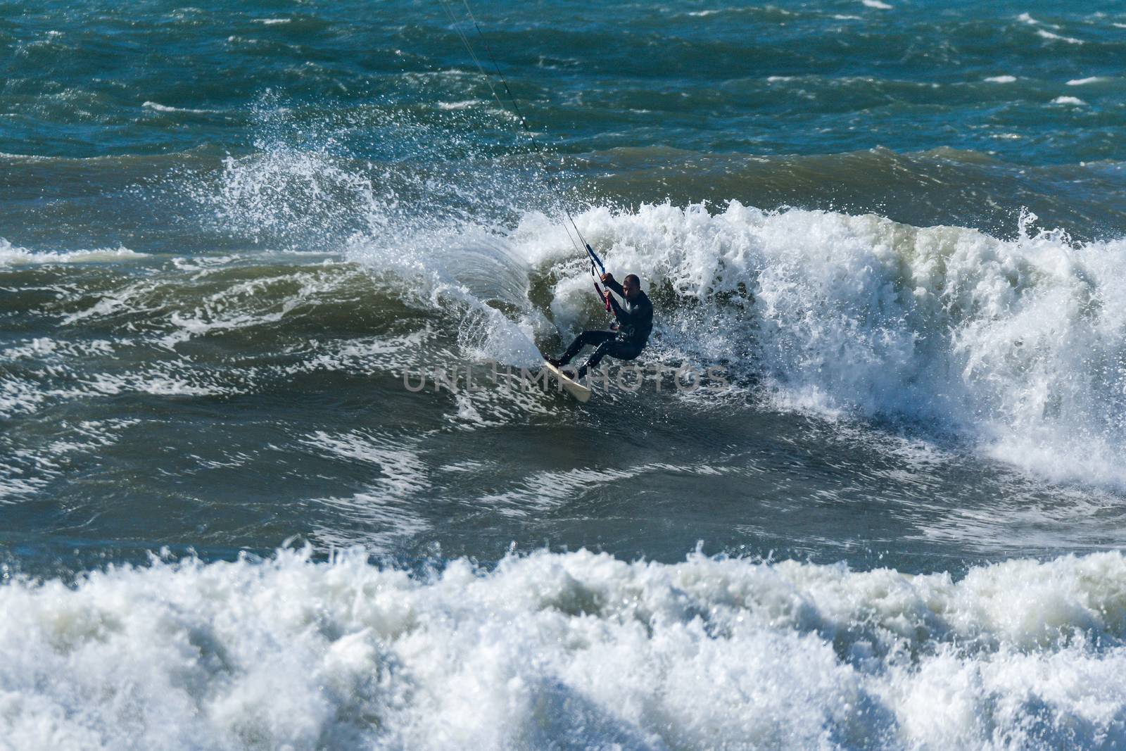Kitesurfer riding ocean waves on a bright sunny day.