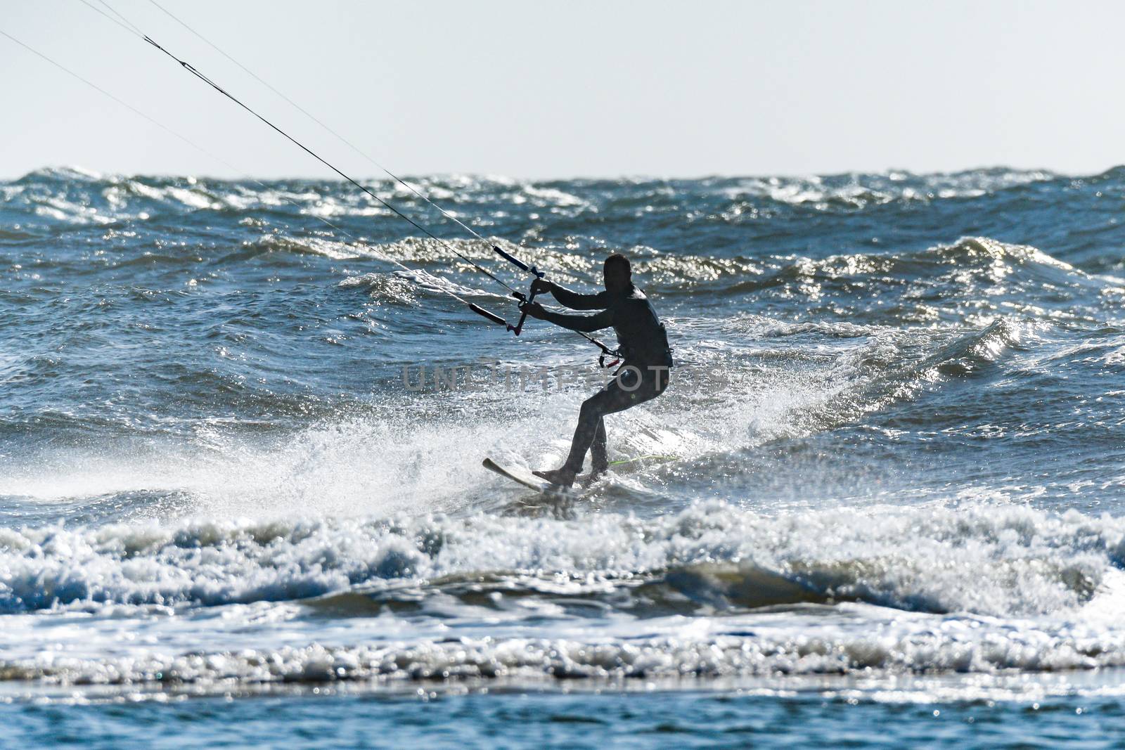 Kitesurfer riding ocean waves on a bright sunny day.