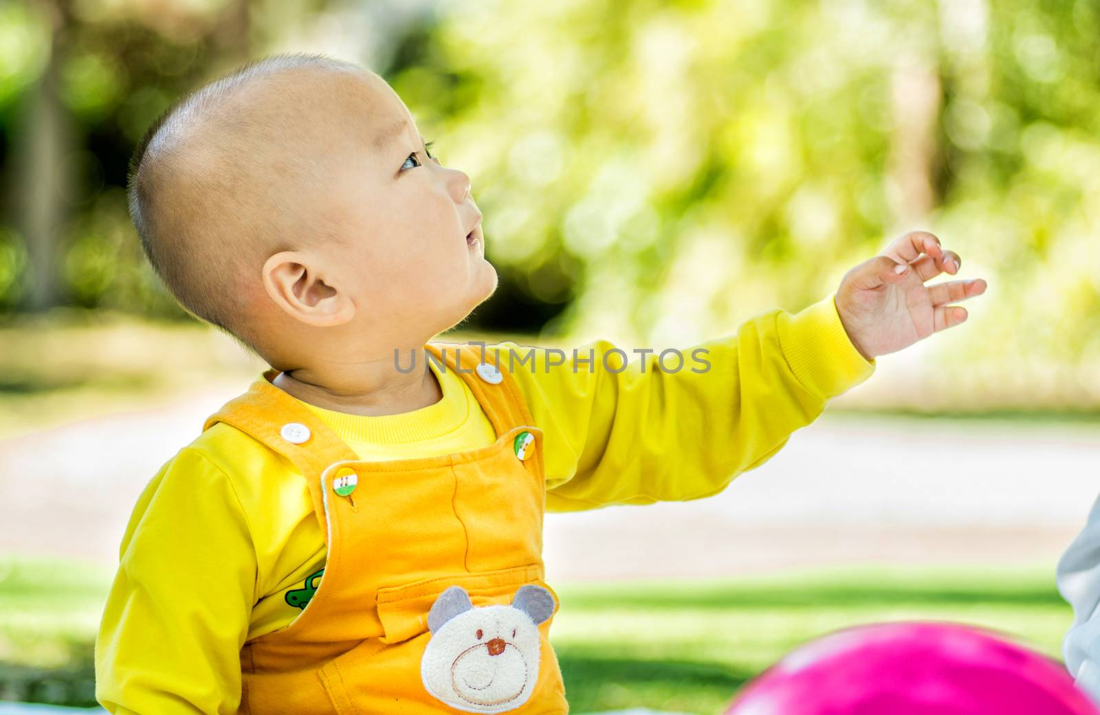 a baby sits on the mat in the park stretching a hand