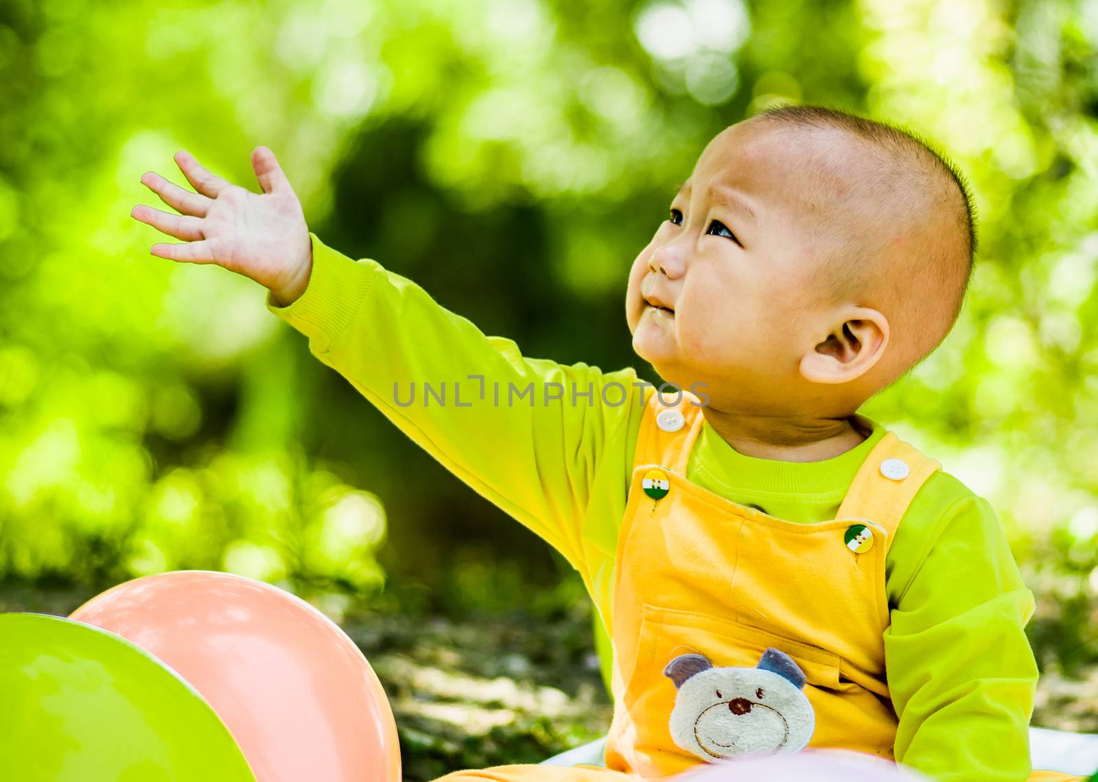 a baby sits on the mat in the park stretching a hand