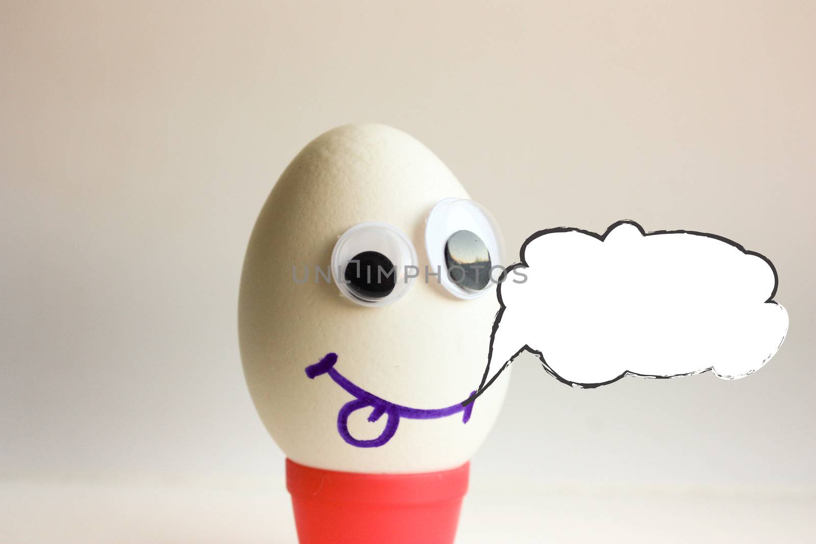 An egg to show the tongue. Egg with a funny painted face on a white background. Photo for your design. With a cloud of thought. Place for text