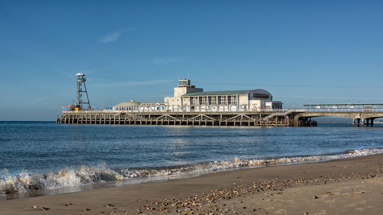 Bournemouth pier from a low angle showing breaking waves on the shore line and a deserted beach