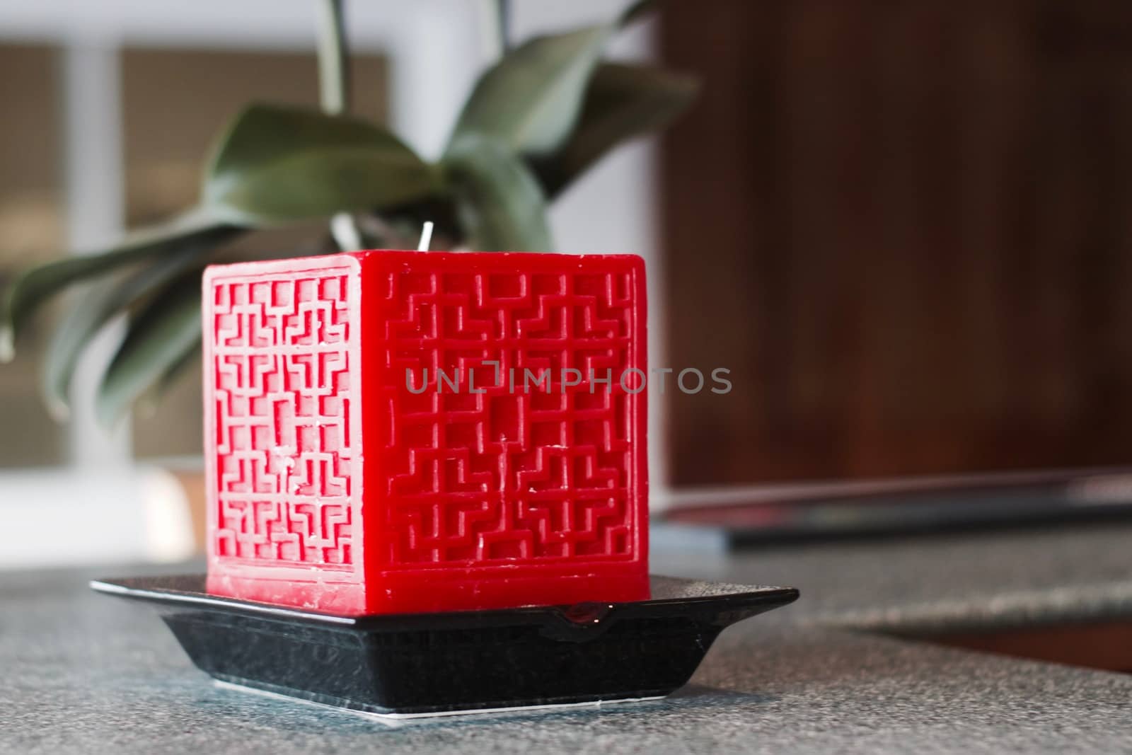 Big red square candle on the black plate with symetric pattern on front.