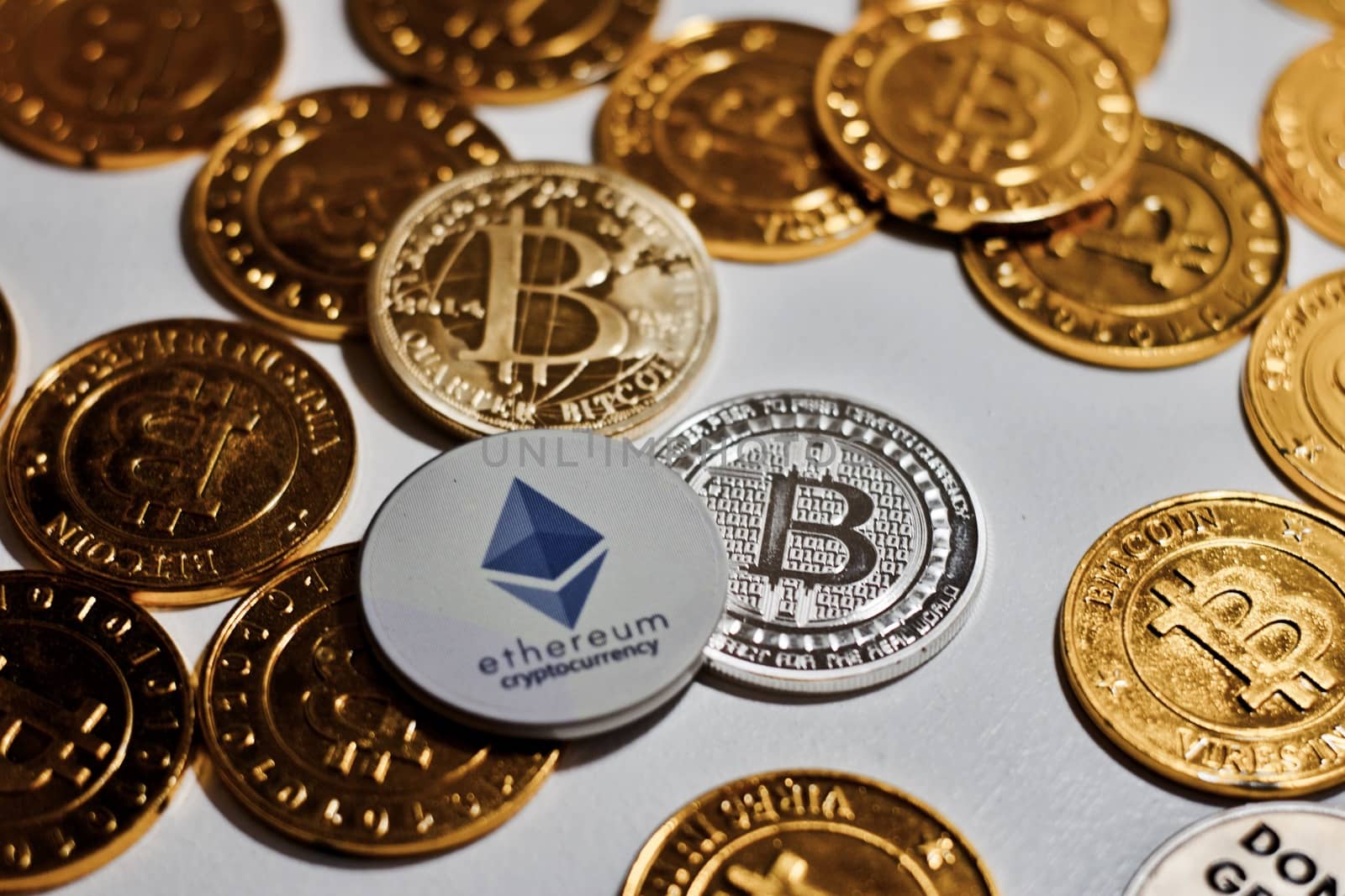 Digital currency physical grey Ethereum coin near gold bitcoins.
