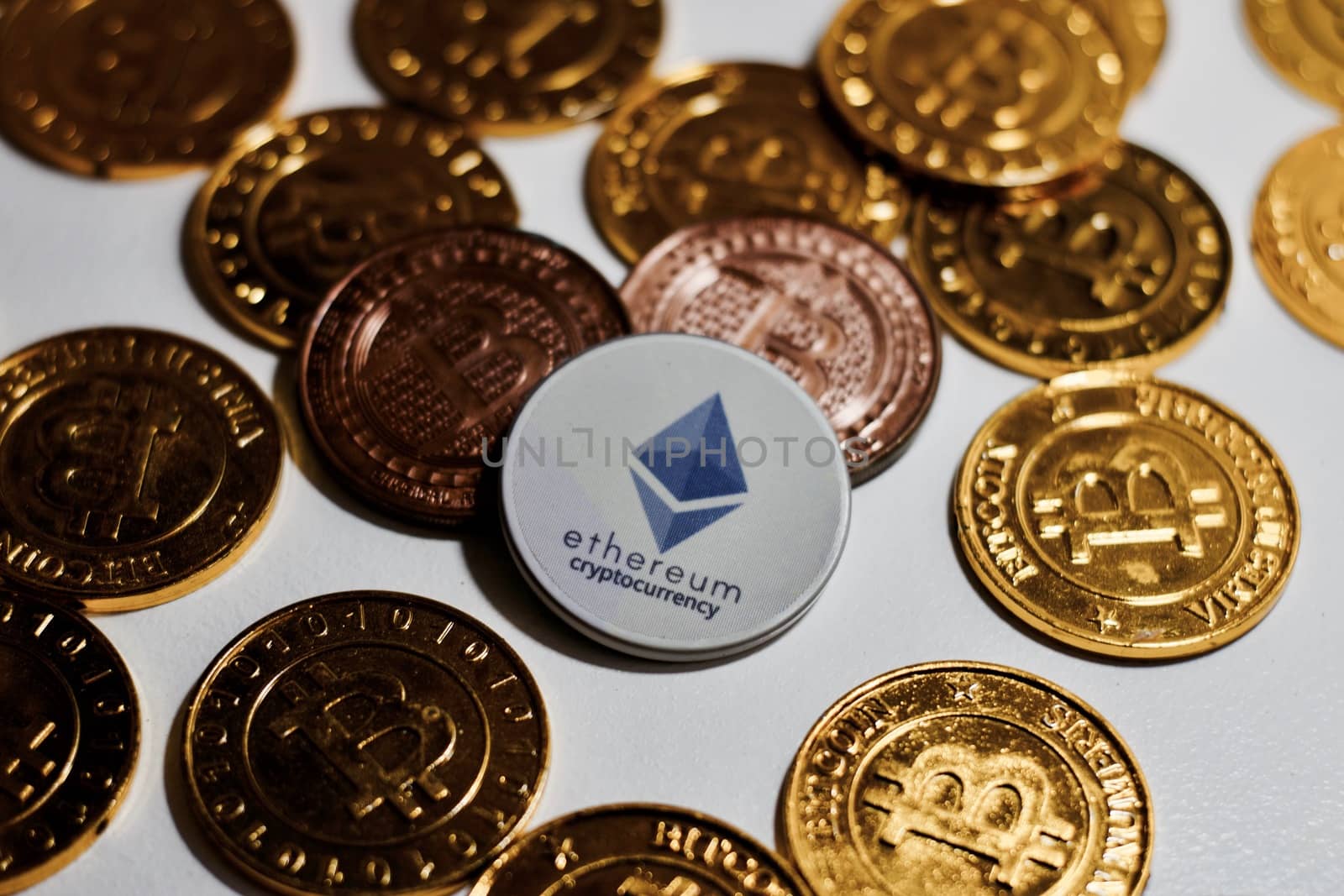 Digital currency physical grey Ethereum coin near gold bitcoins.