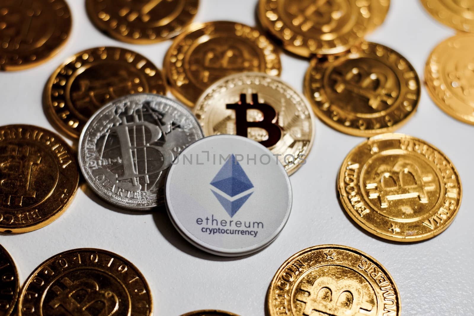 Digital currency physical grey Ethereum coin near gold bitcoins.