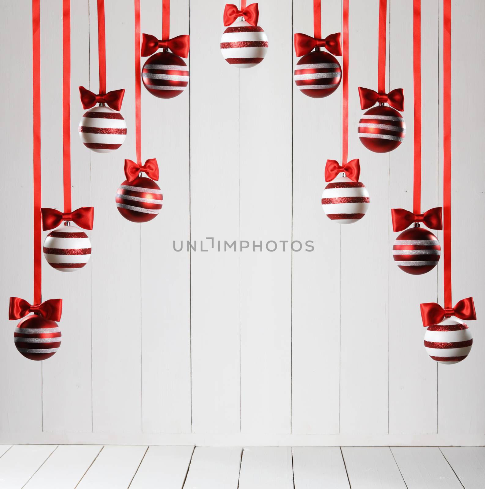 Red Christmas balls hanging on red ribbons on white wooden background