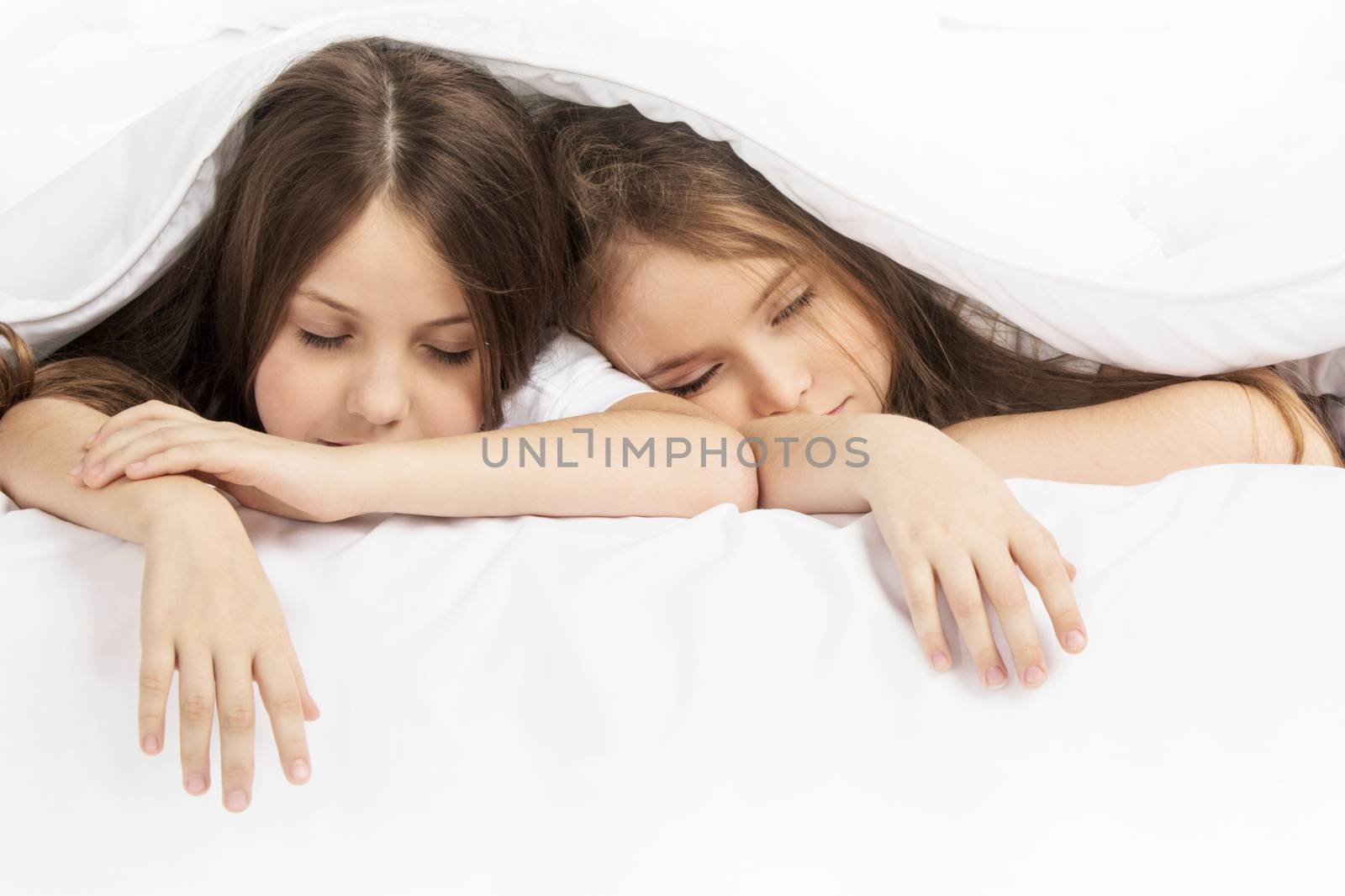 Two beautiful children sleeping in bed under one white blanket