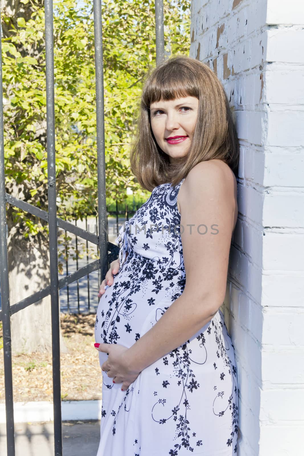 Pregnant woman in sunlight near white brick wall