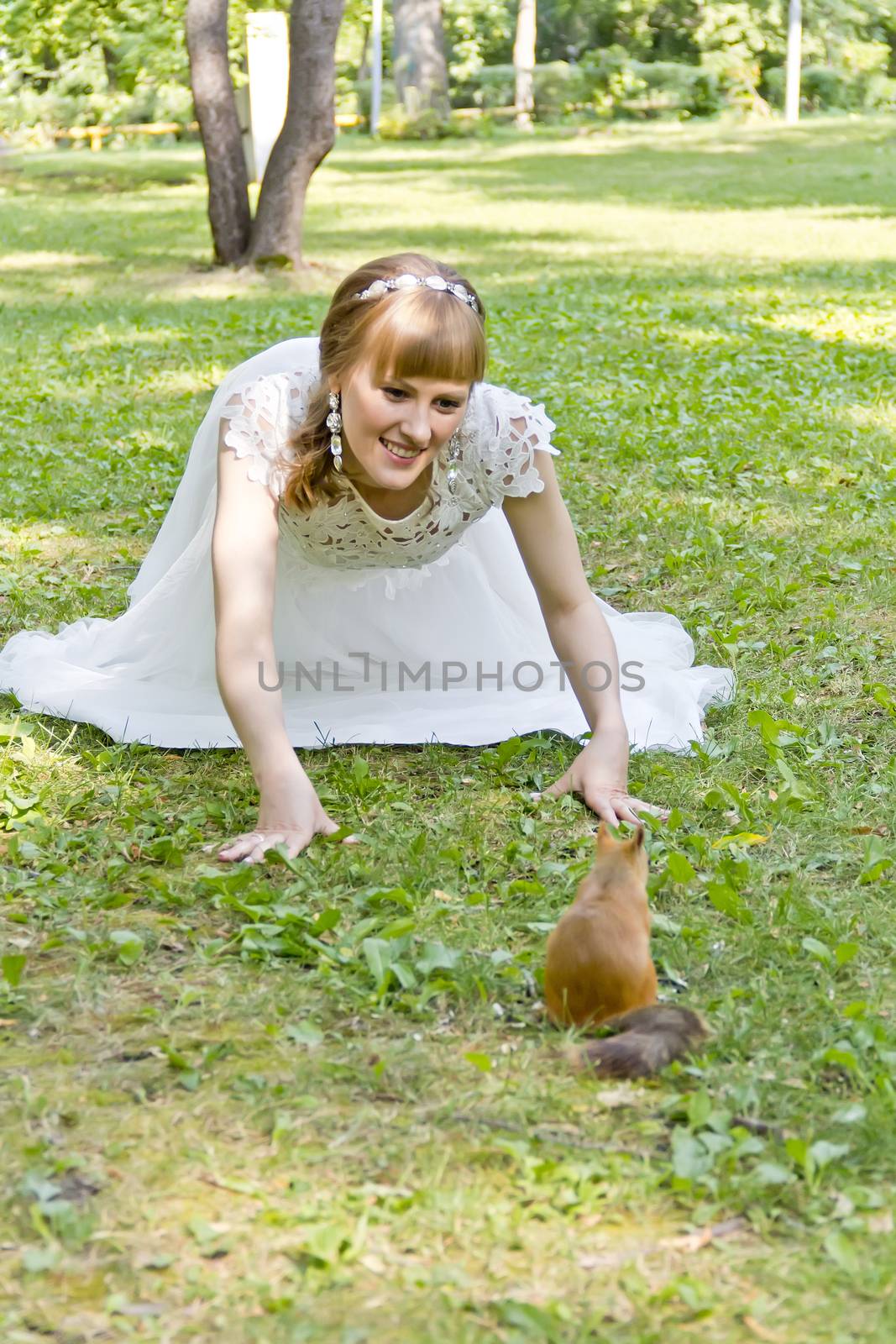 Bride in white lying on grass next to the squirrel by Julialine