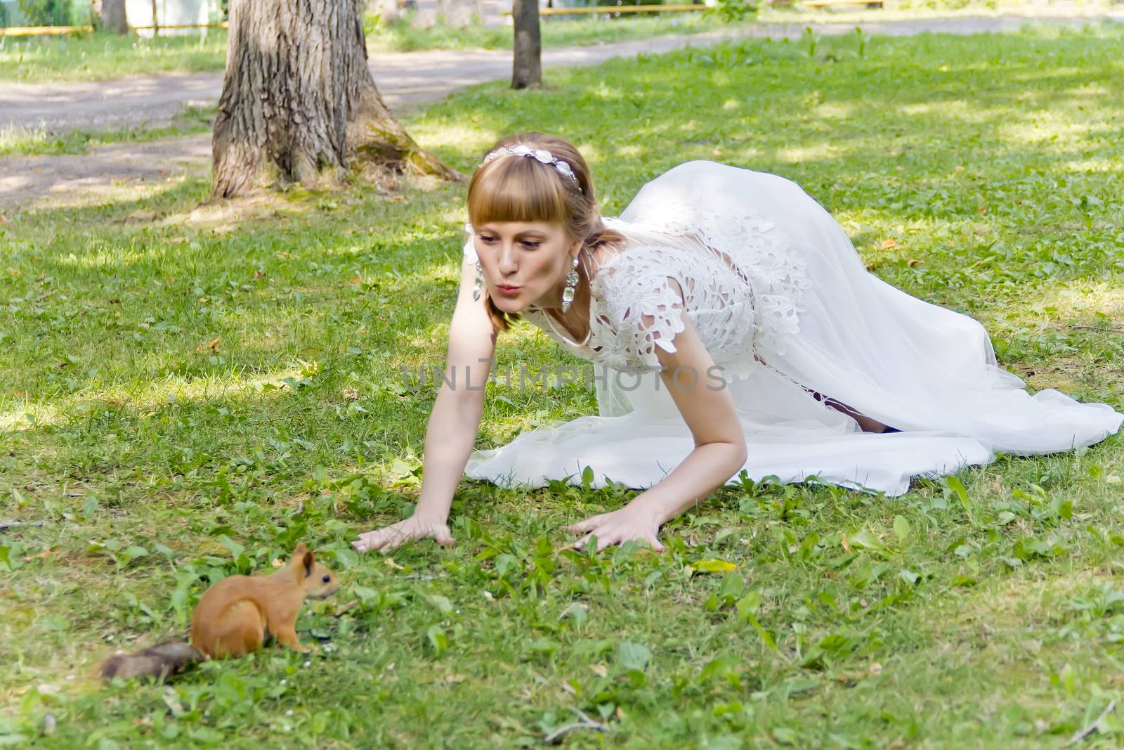 Bride in white lying on green grass next to the squirrel in summer