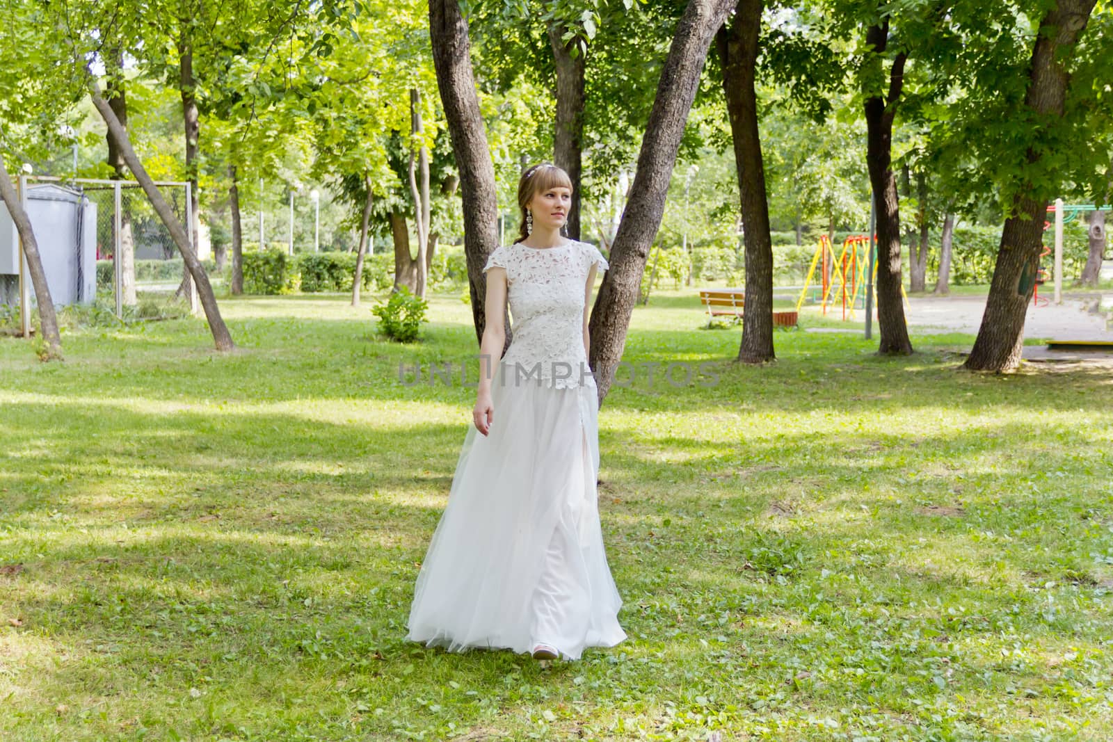 Bride in white lace dress walking in summer park