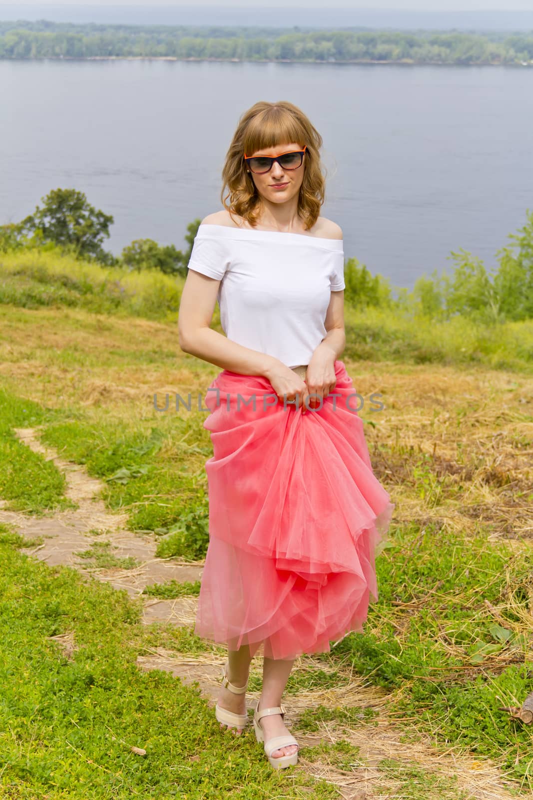 Young girl in sunglasses and pink skirt walking on river embankment