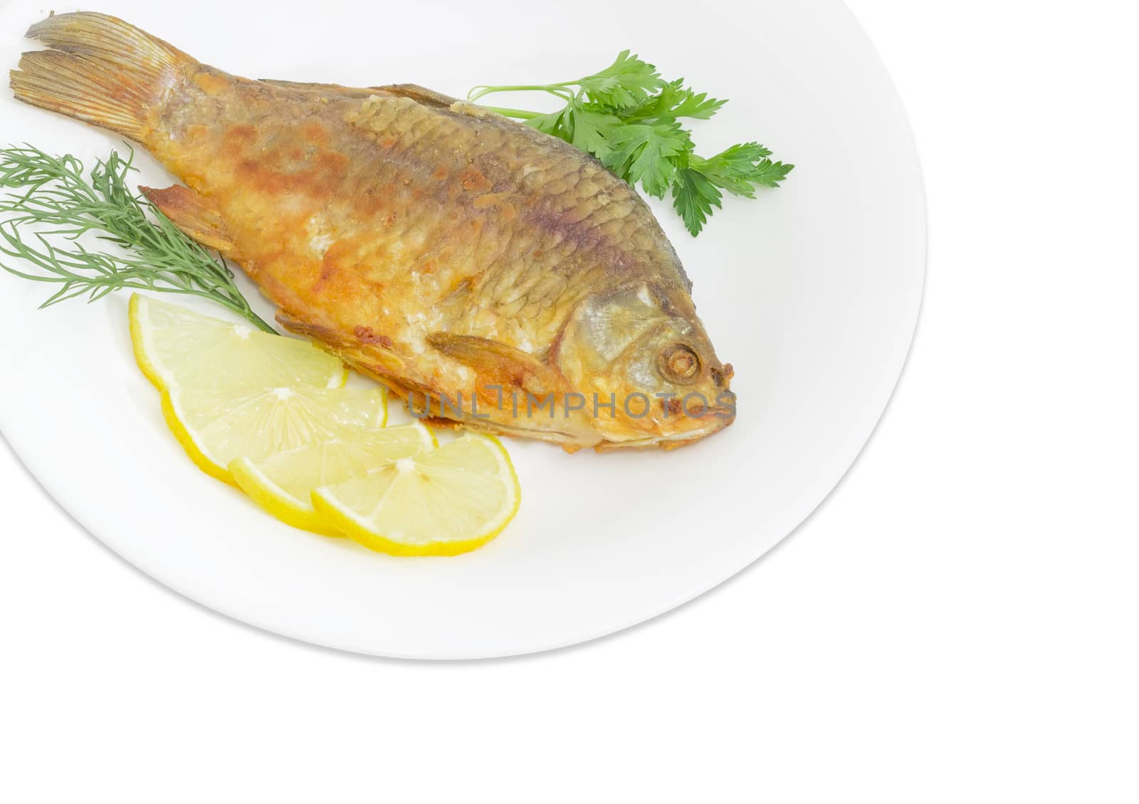 Fragment of a white dish with fried crucian, slices of the lemon, twigs od the parsley and dill on a white background
