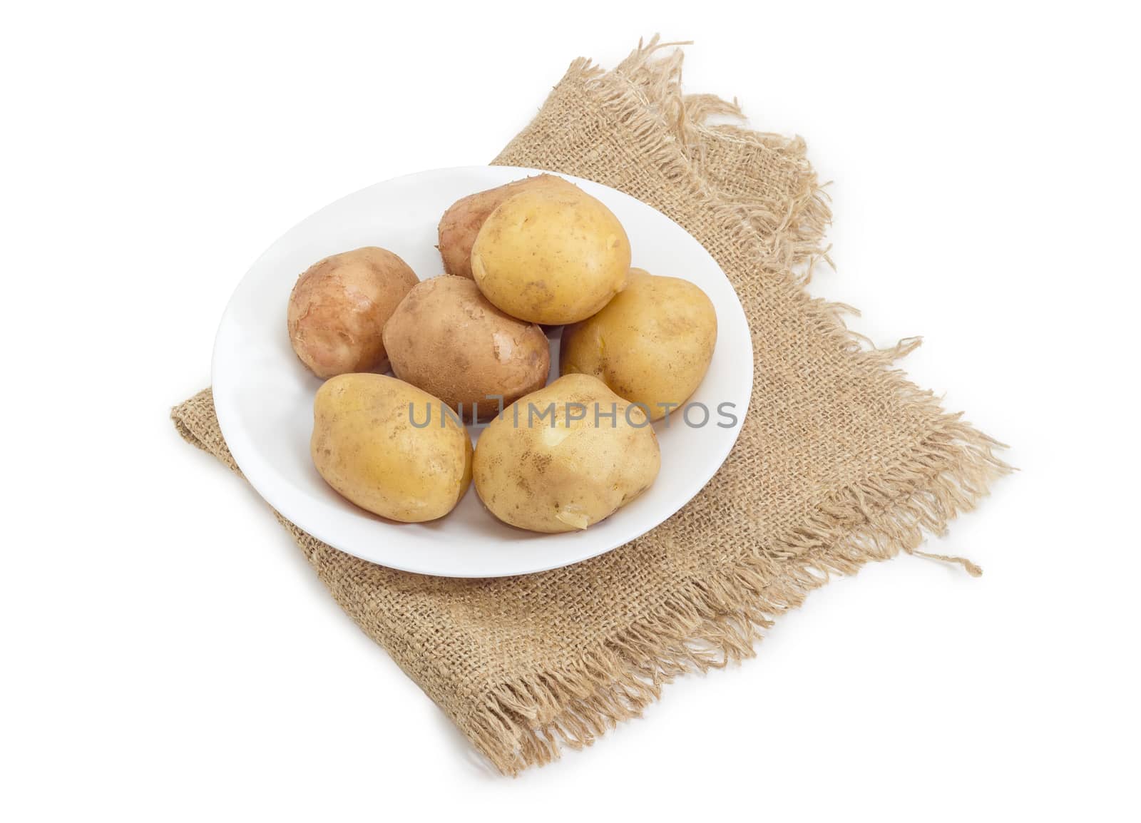 Several whole potatoes boiled in their jackets on the white dish on a sackcloth on a white background
