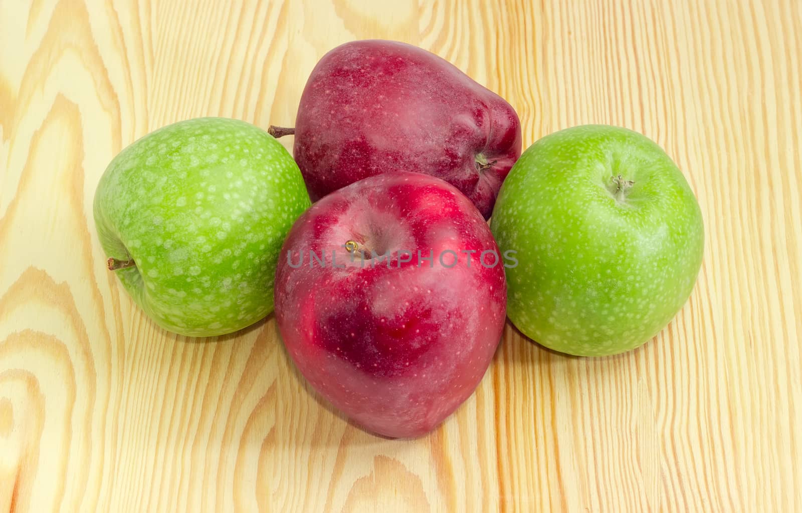 Two green and two dark red freshly harvested ripe apples on a light wooden surface
