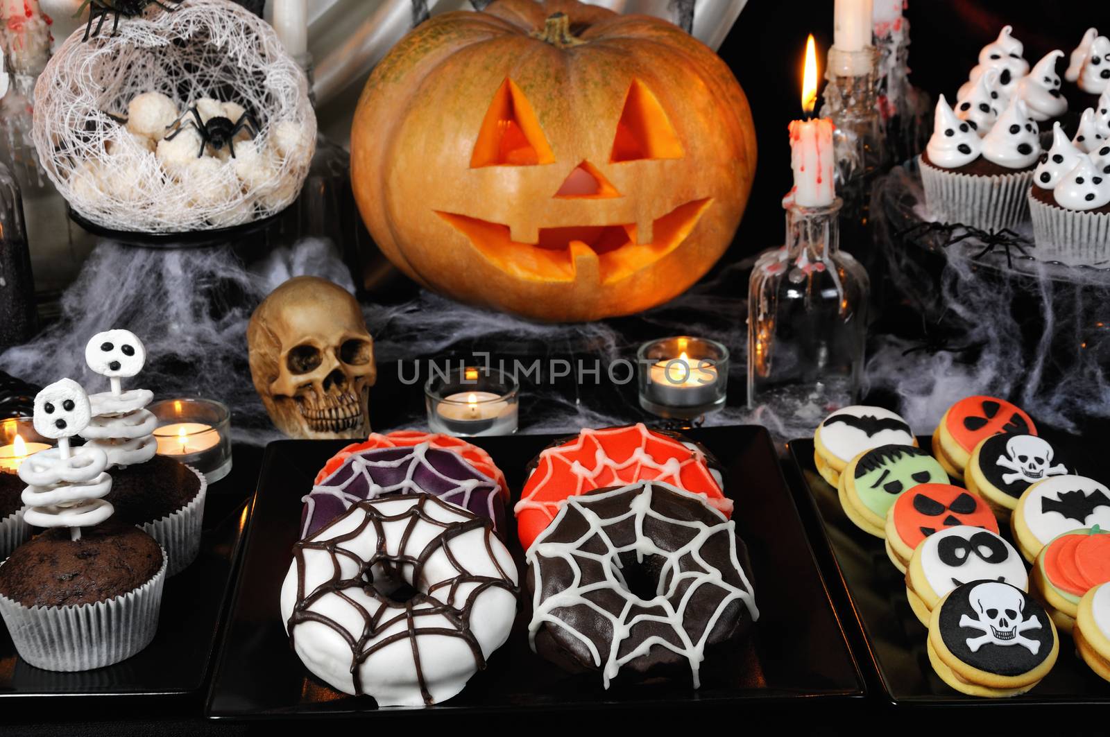 Dishes with glazed donuts, muffins with skeletons, cookies with marzipan on a Halloween table