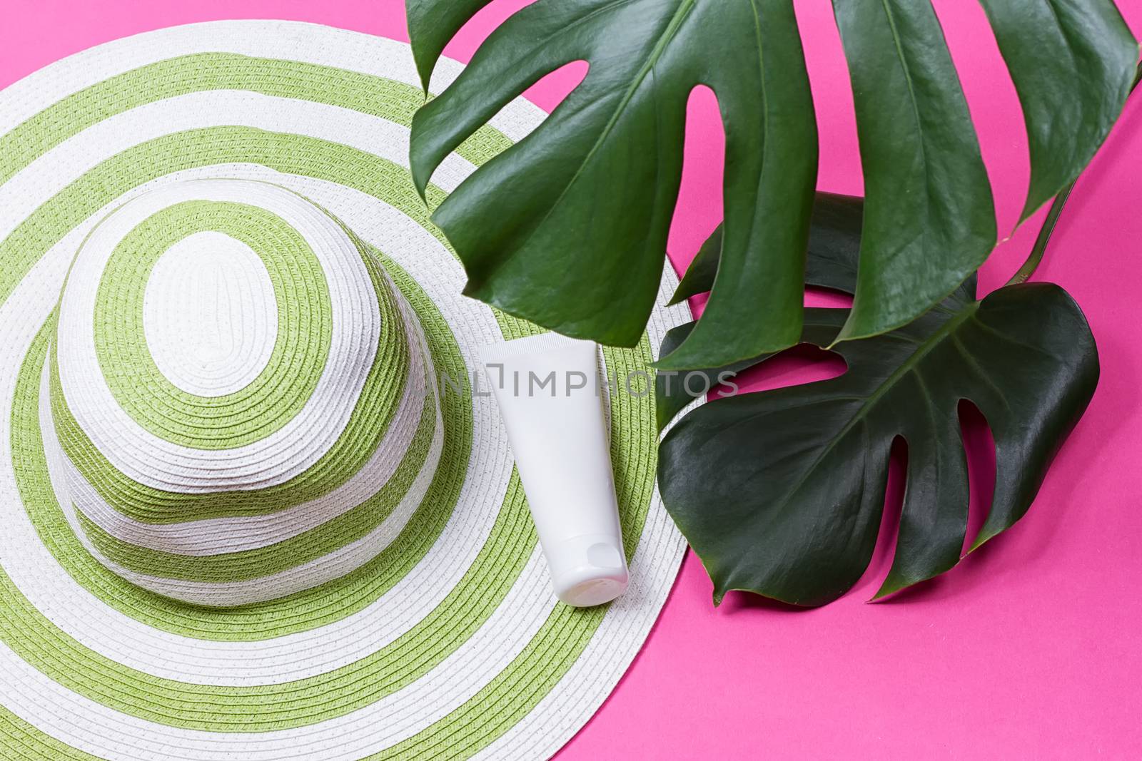 on green monstera leaf with sunglasses and straw hat on pink marble table