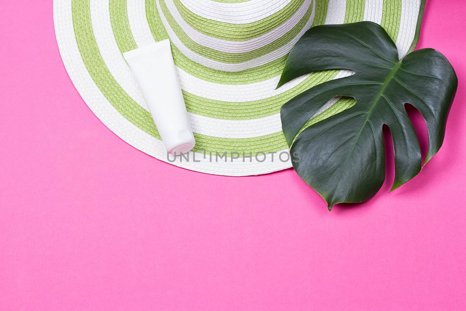 on green monstera leaf with sunglasses and straw hat on pink marble table