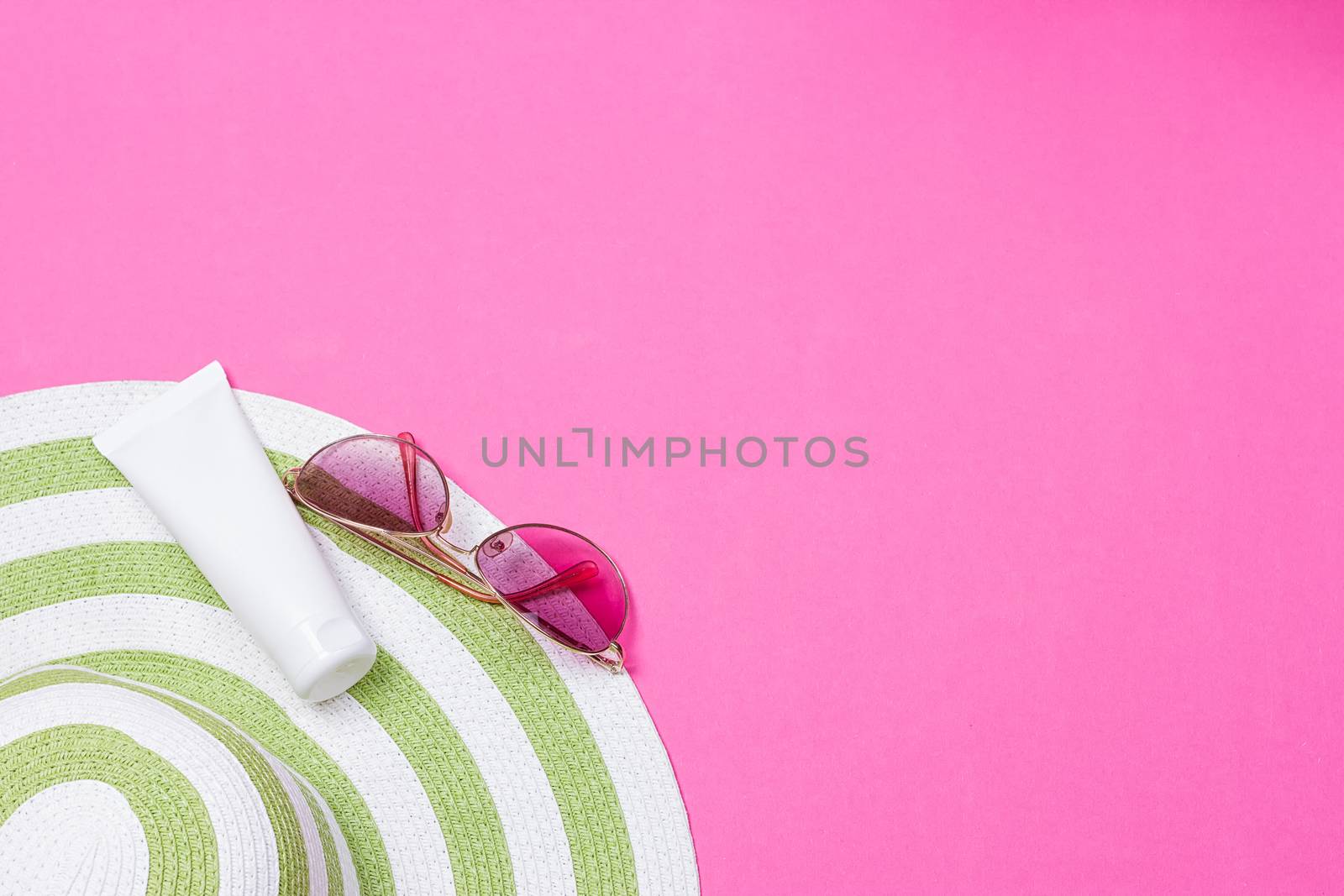 Straw hat and sun block lotion tube and sunglasses on a pink background