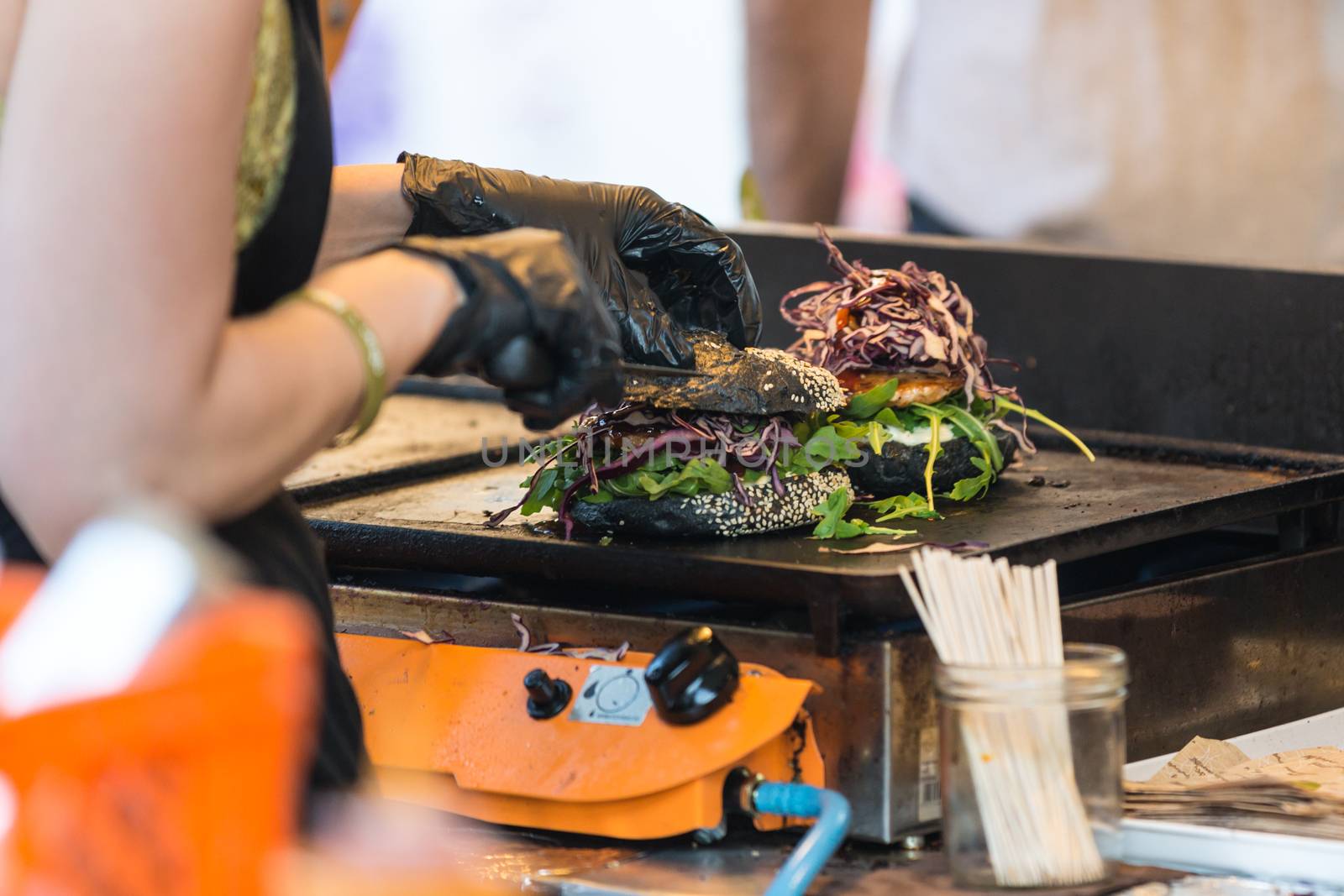 Chef making beef burgers outdoor on open kitchen international food festival event. Street food ready to serve on a food stall.