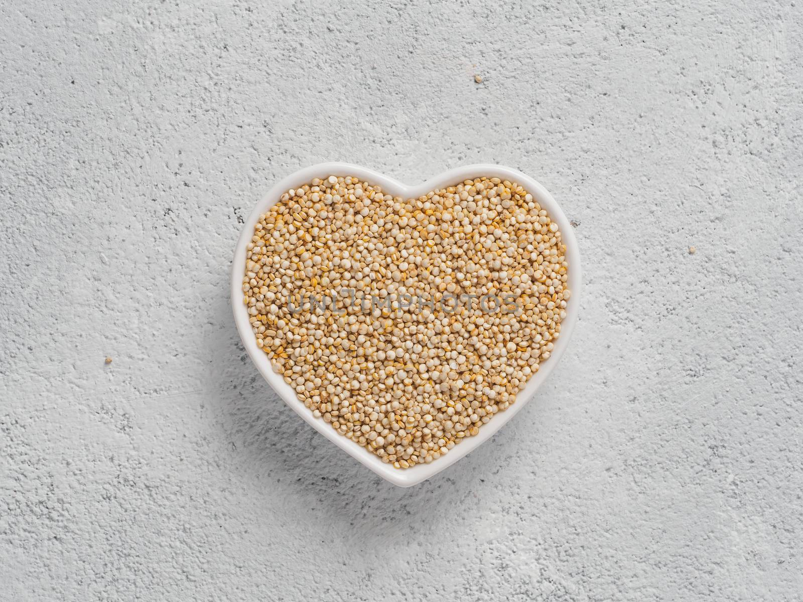 Quinoa in heart-shaped bowl on gray cement background. Gluten free ancient grain for healthy diet. I love quinoa concept. Copy space.