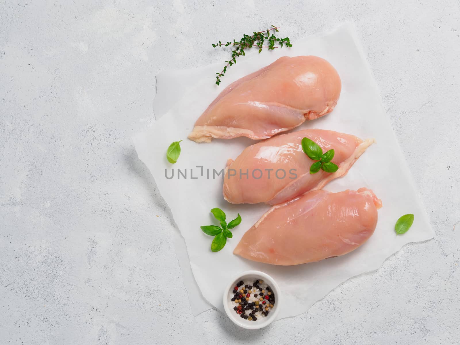 Raw chicken breast with fresh basil on white paper. Raw chicken fillet on gray cement background. Copy space. Top view or flat lay.