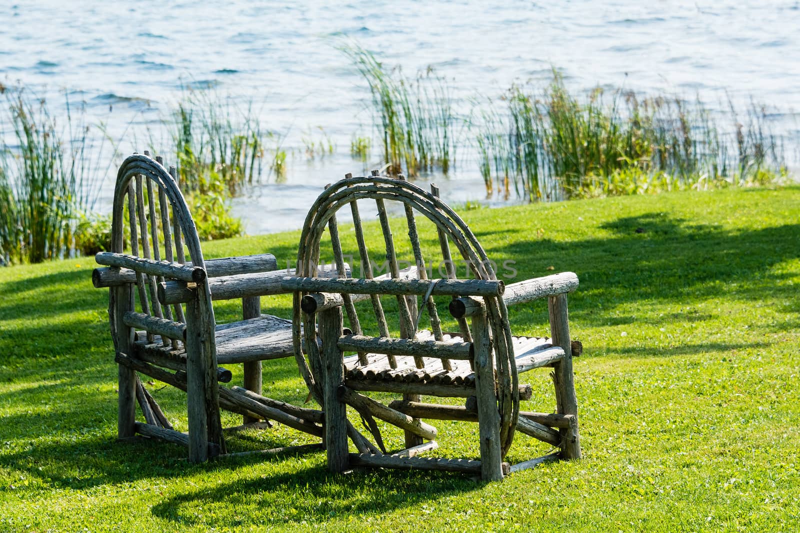 Two old wooden chairs rudely made stand  side by side on a green lawn
