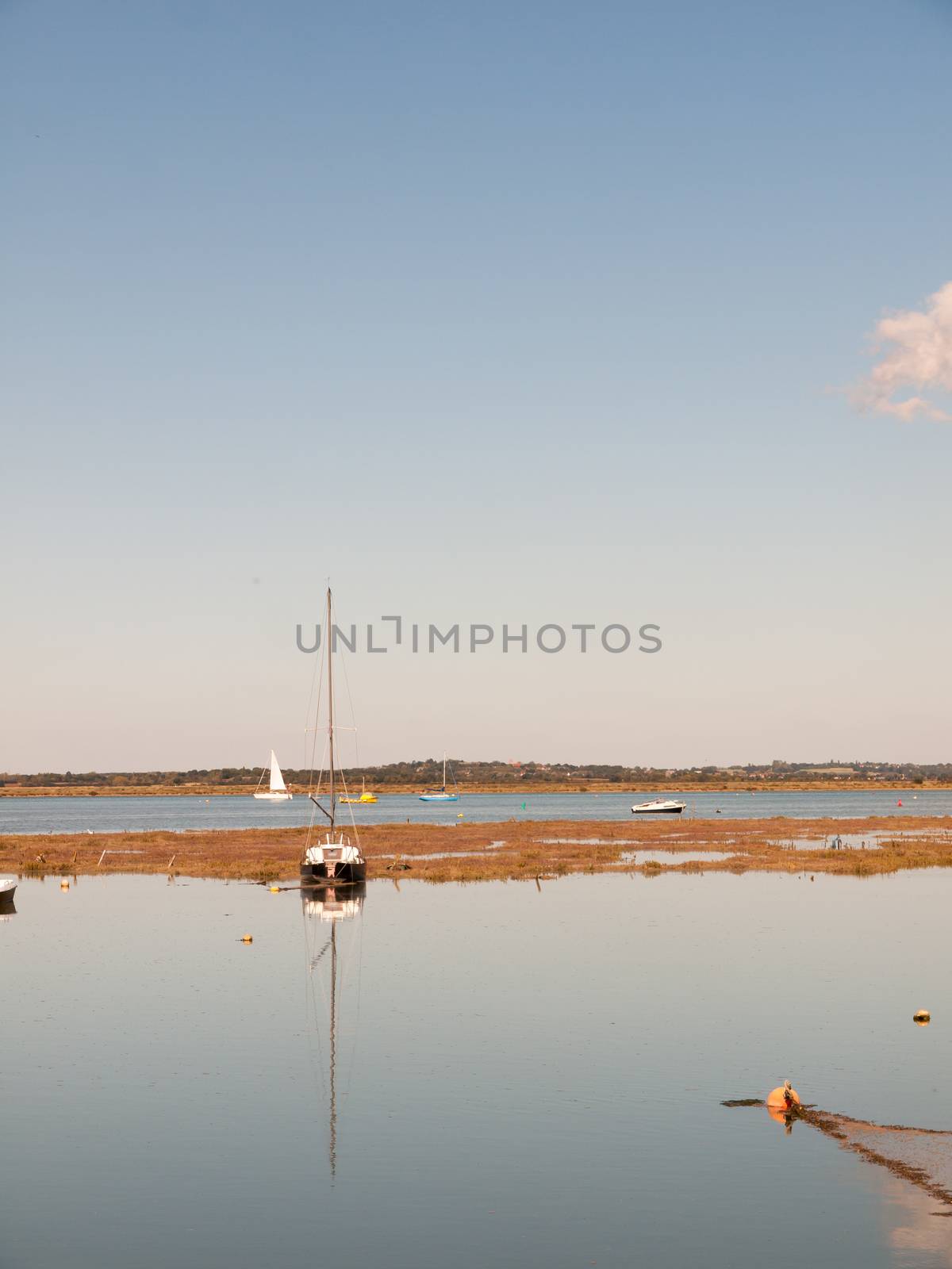 boat moored in estuary scene with mast reflected in water blue sky; essex; england; UK