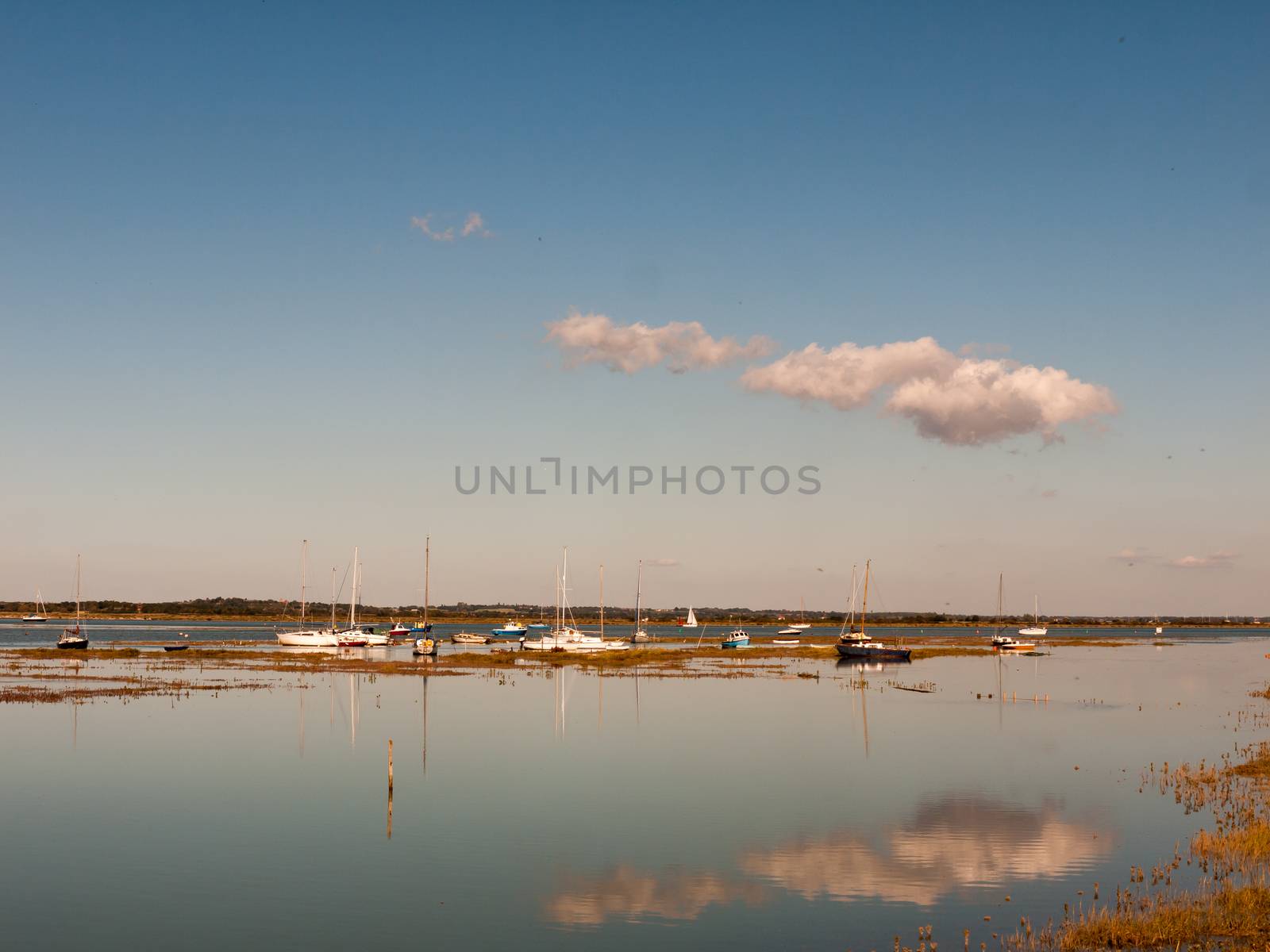 beautiful estuary scene with blue sky moored boats, masts, and reflection of cloud in water surface; essex; england; UK