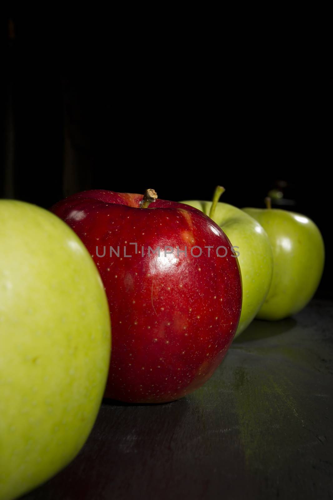 Red apple standing out in a row of green apples