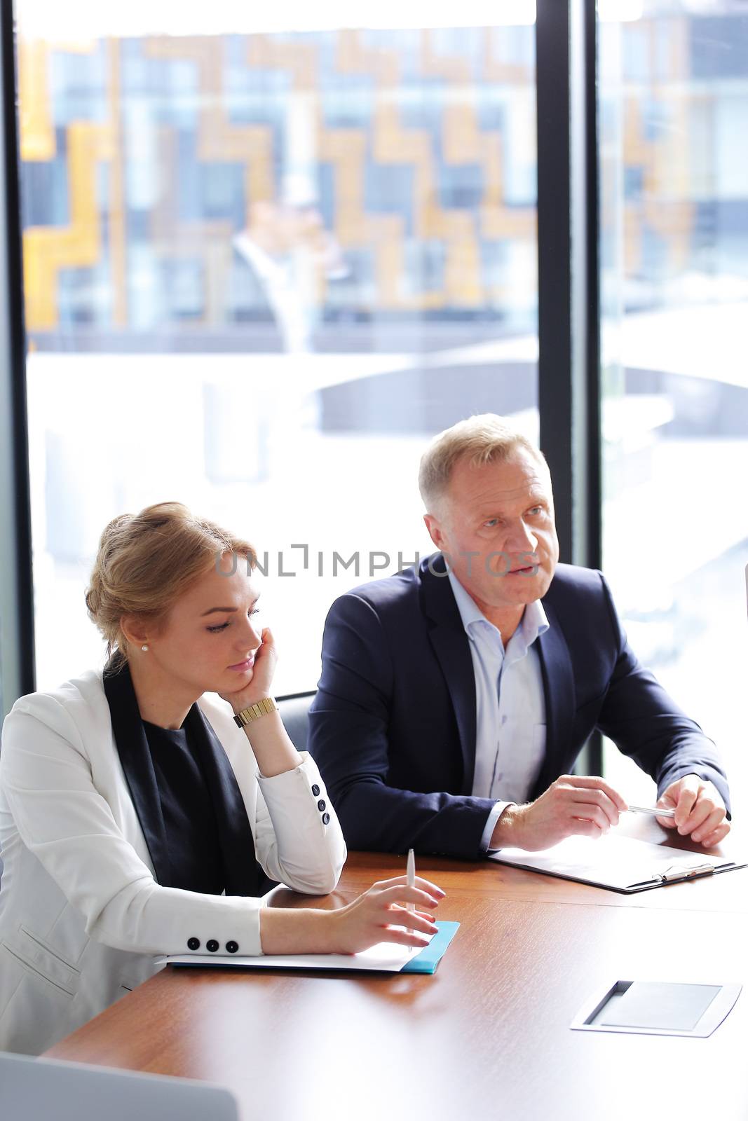 Mature business man and his young female assistant sitting at meeting table in office