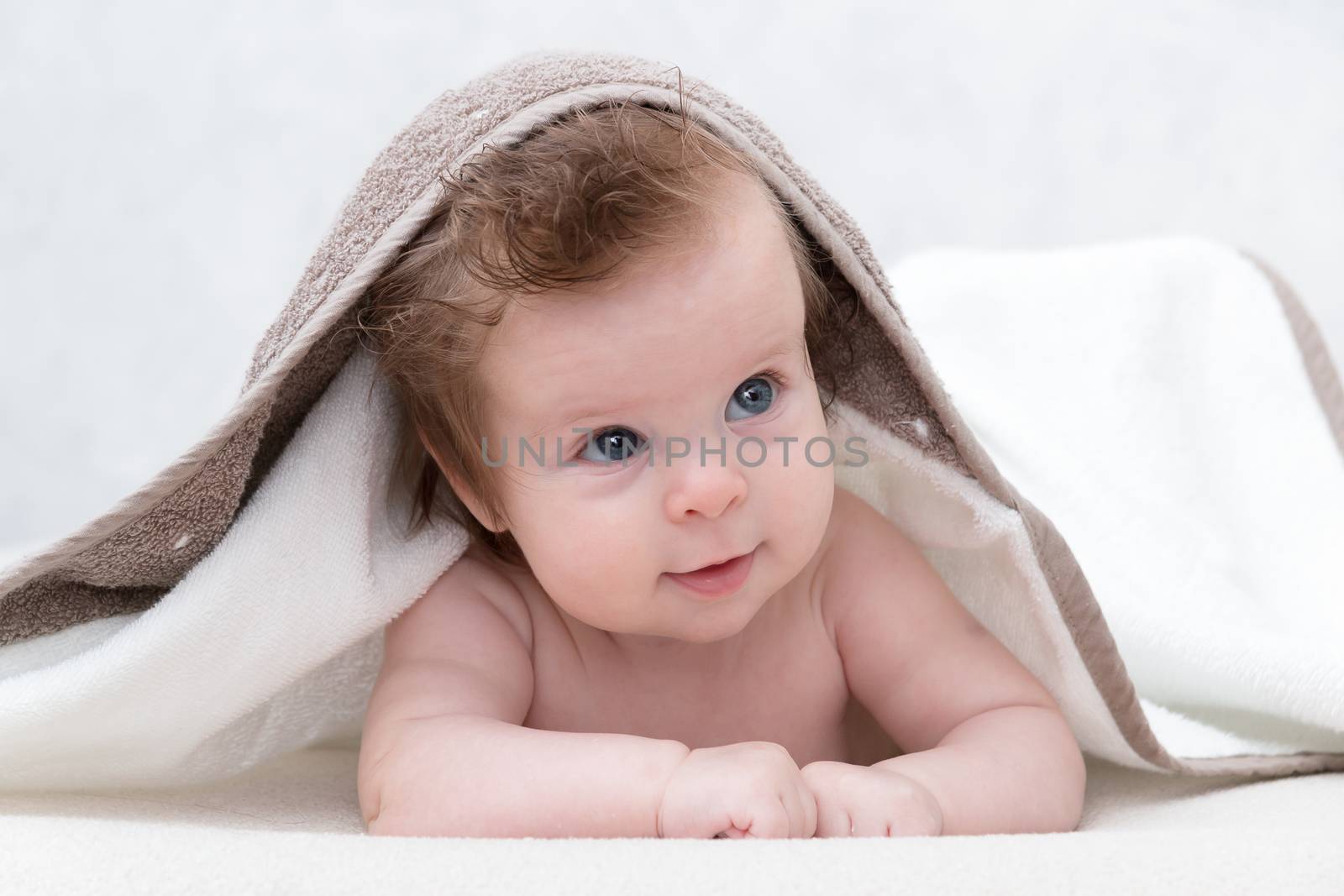 Smiling baby boy after shower or bath with towel on head. Happy laughing baby wearing hooded towel lying on parents bed after bath or shower. Clean dry child in bedroom. Bathing and washing of little kids. Children hygiene. Textile for infants.