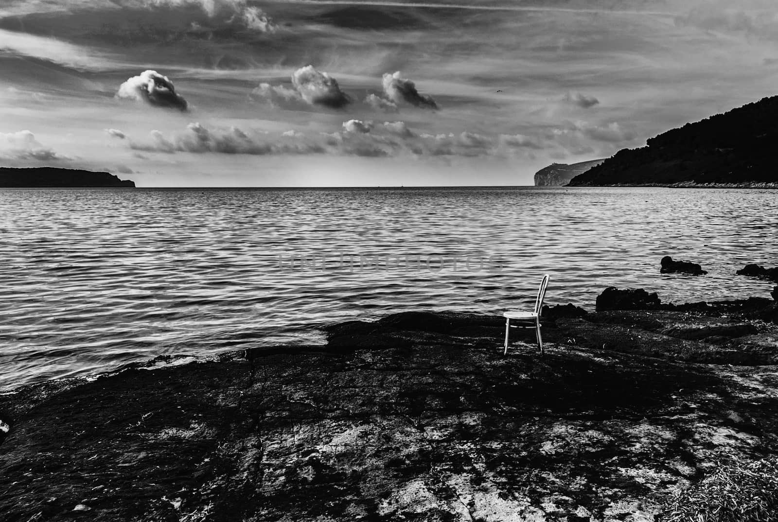 Old iron chair on the sea in black and white with dramatic clouds