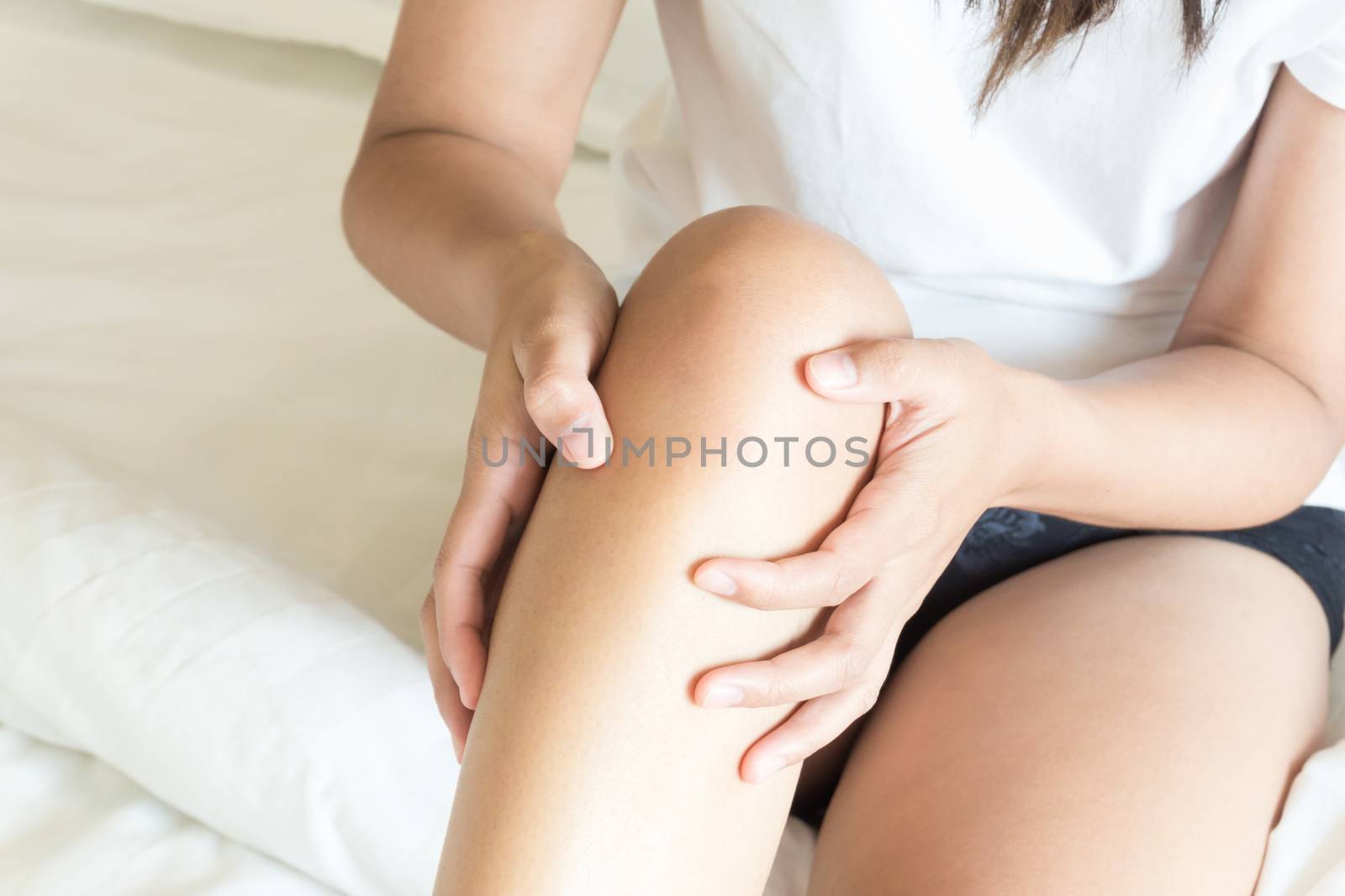 Closeup woman hand holding knee with pain on bed, health care and medical concept