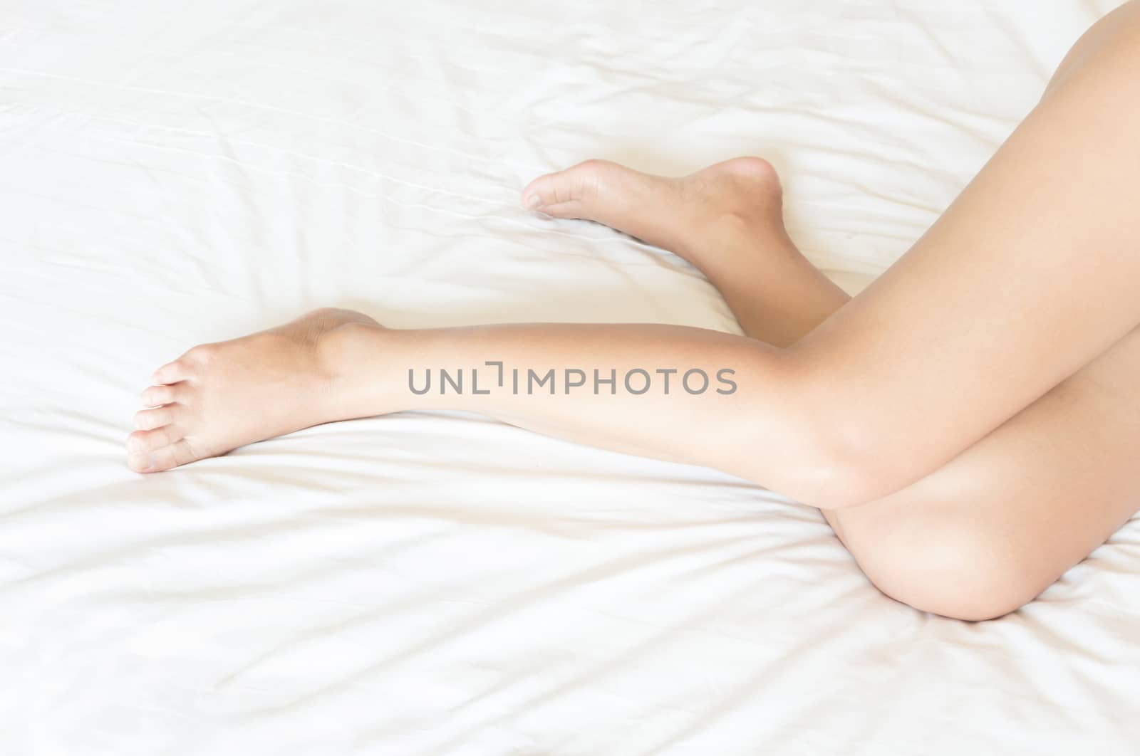 Closeup woman legs with sleeping on white bed, beauty and skin care concept, selective focus