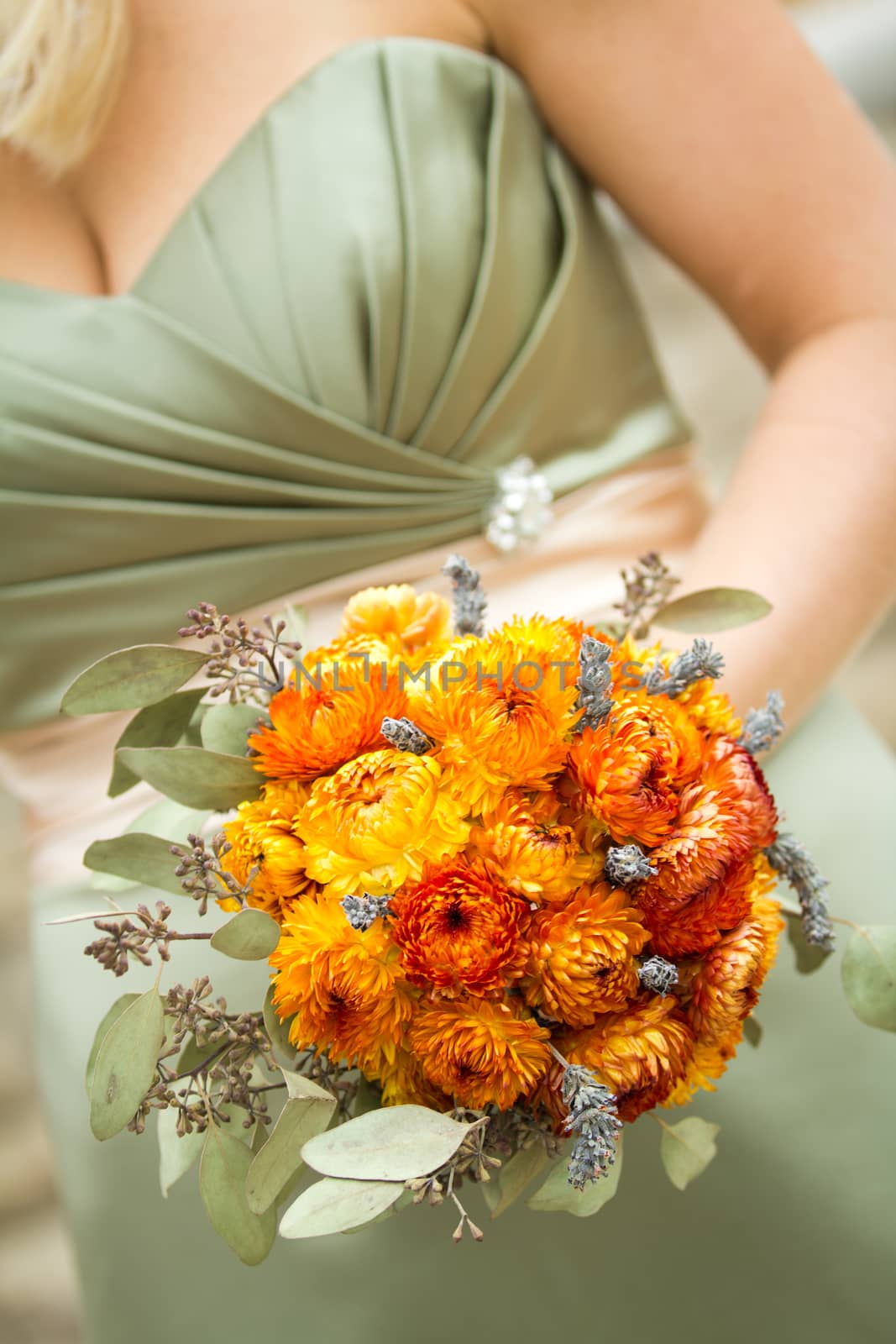 Orange bouquet being held by bridesmaid wearing a green dress.