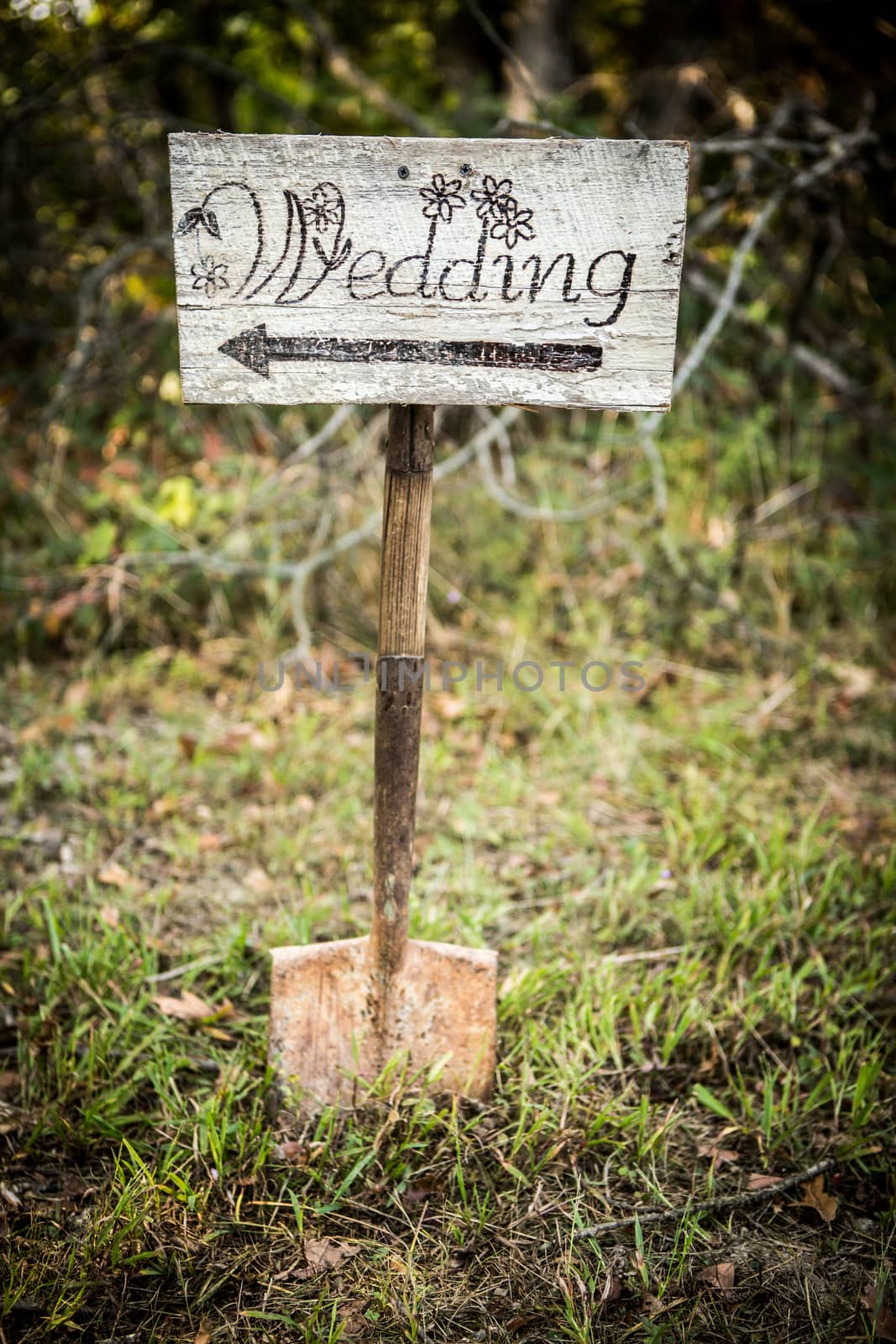Homemade rustic wedding sign placed on a shovel in the woods. Arrow points right.