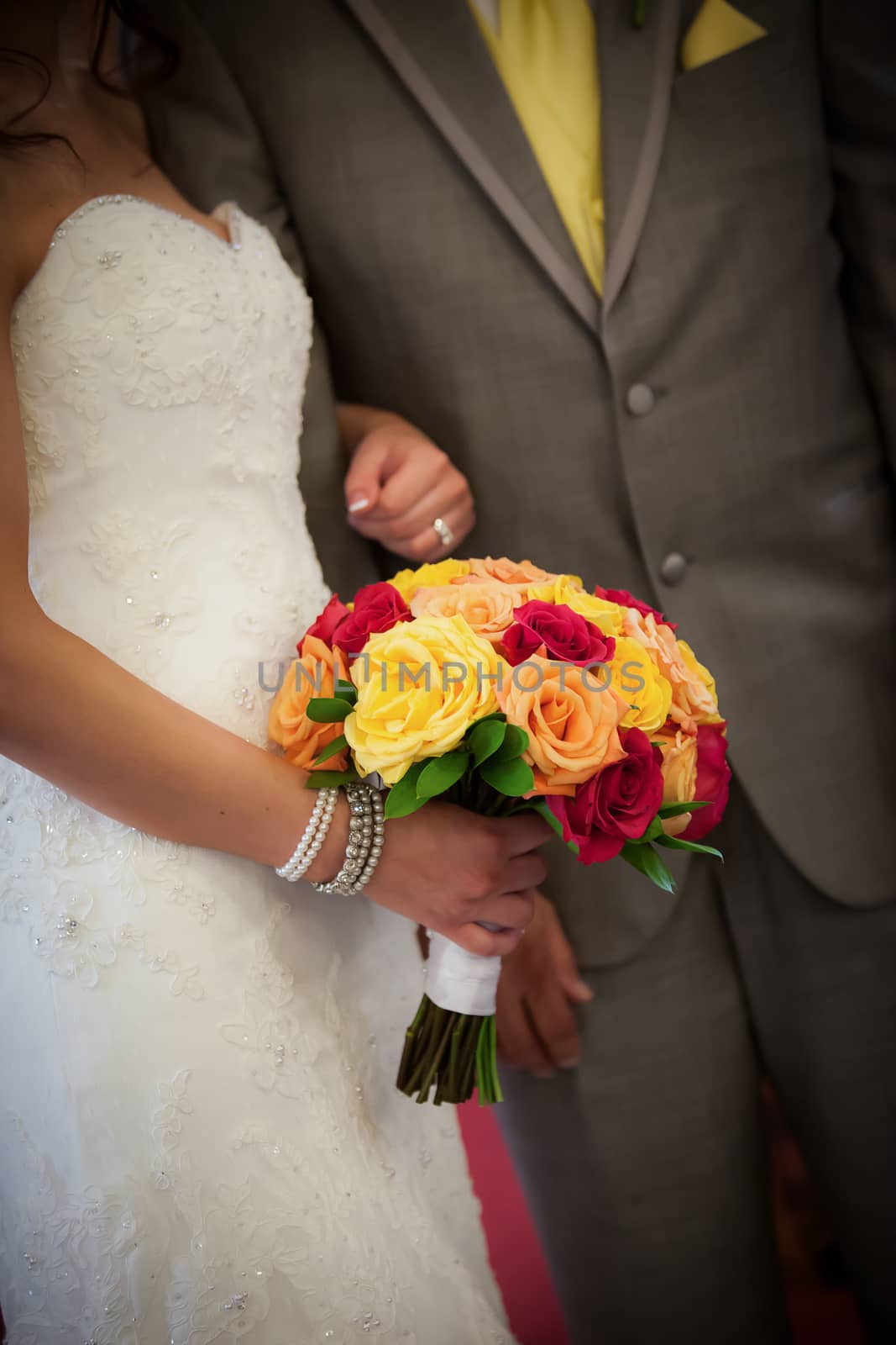 Beautiful bride and groom holding red, yellow, orange bouquet.