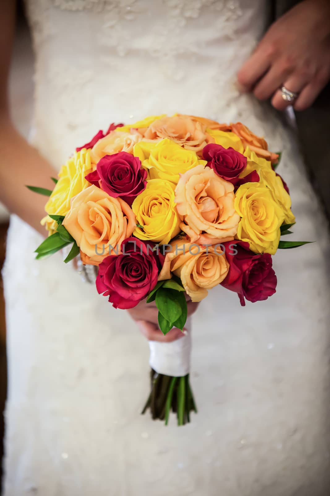 Beautiful bride holding red, yellow, orange bouquet.