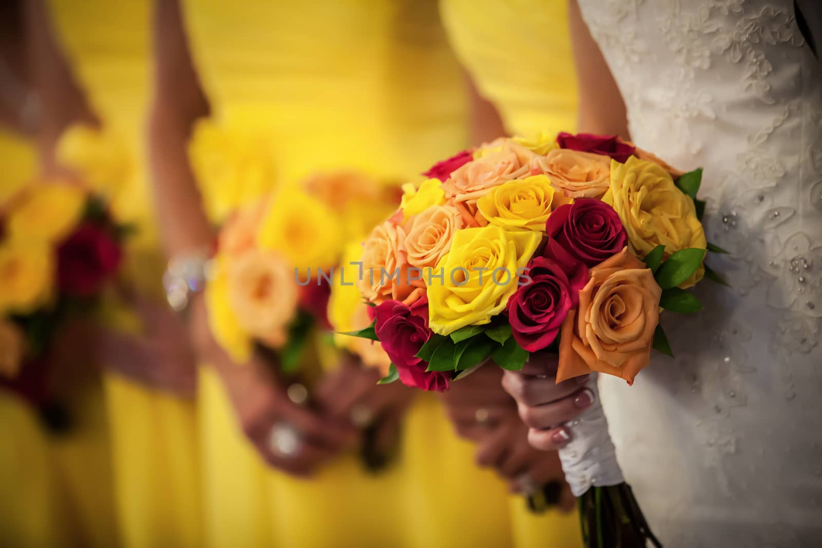 Beautiful bride holding red, yellow, orange bouquet with bridesmaids in the background.
