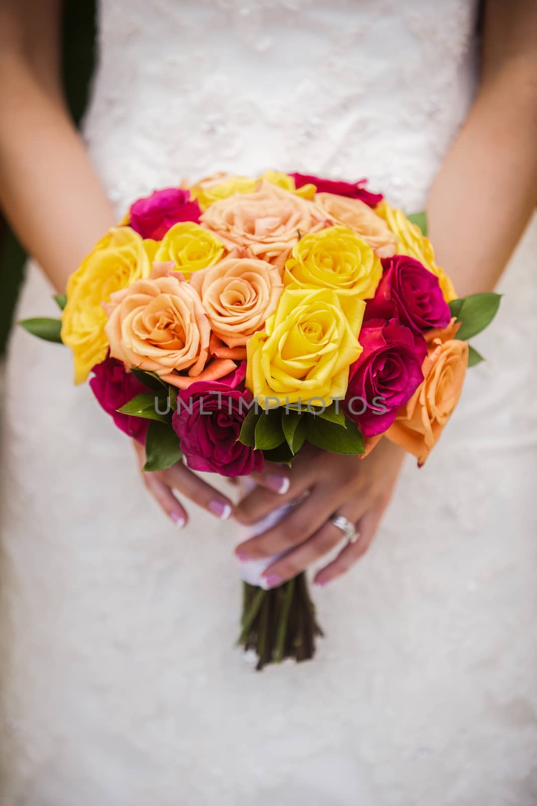Beautiful bride and groom holding red, yellow, orange bouquet.