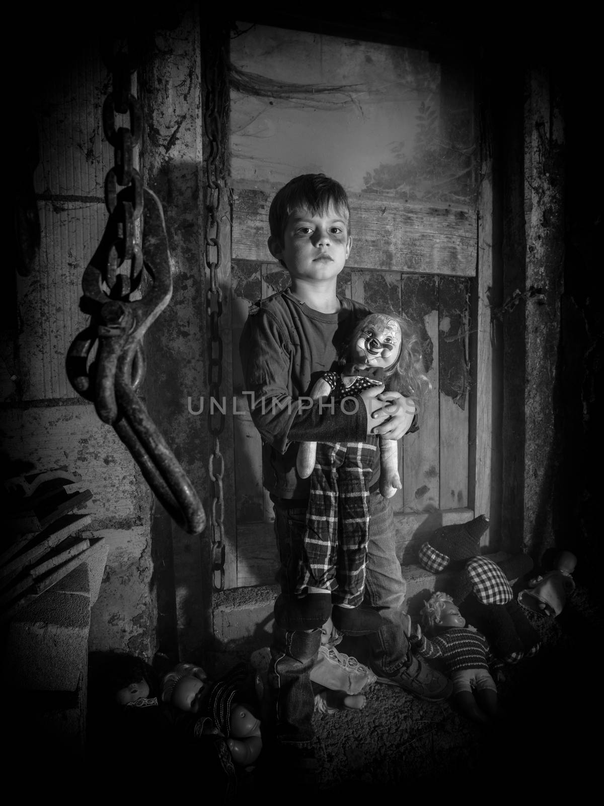 Photo of a creepy young boy holding an old clown doll in an old barn covered in spiderwebs and dust.