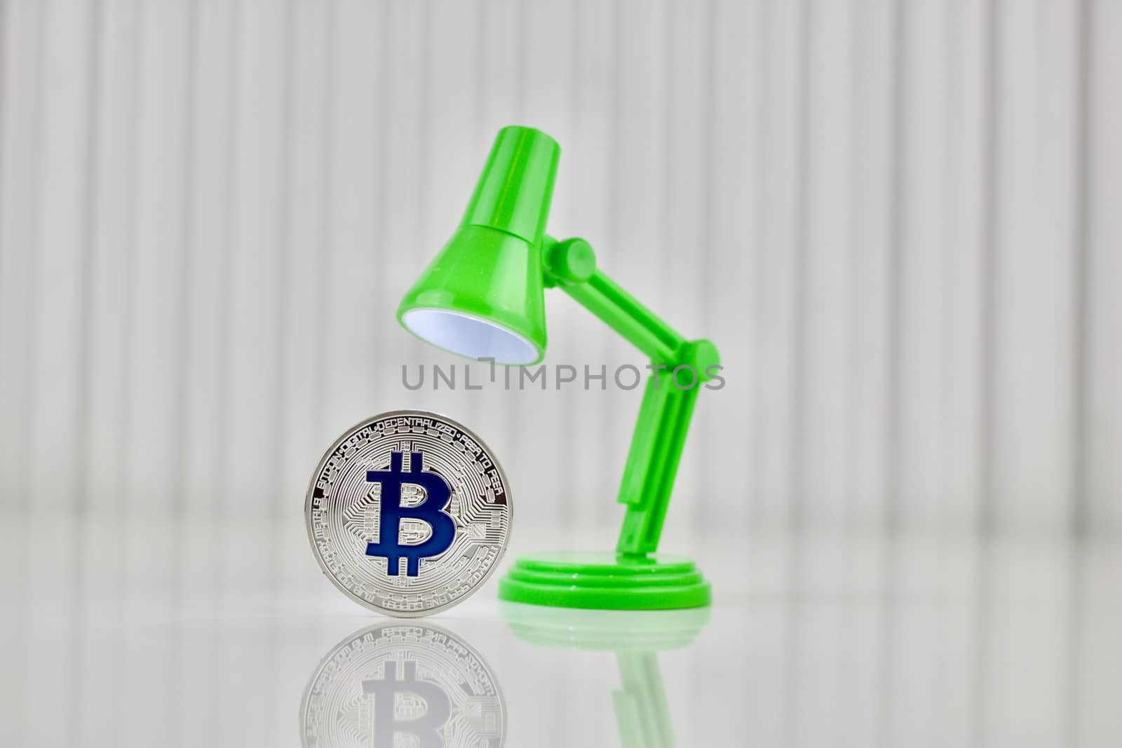 Digital currency physical silver bitcoin coin near green lamp on the table.