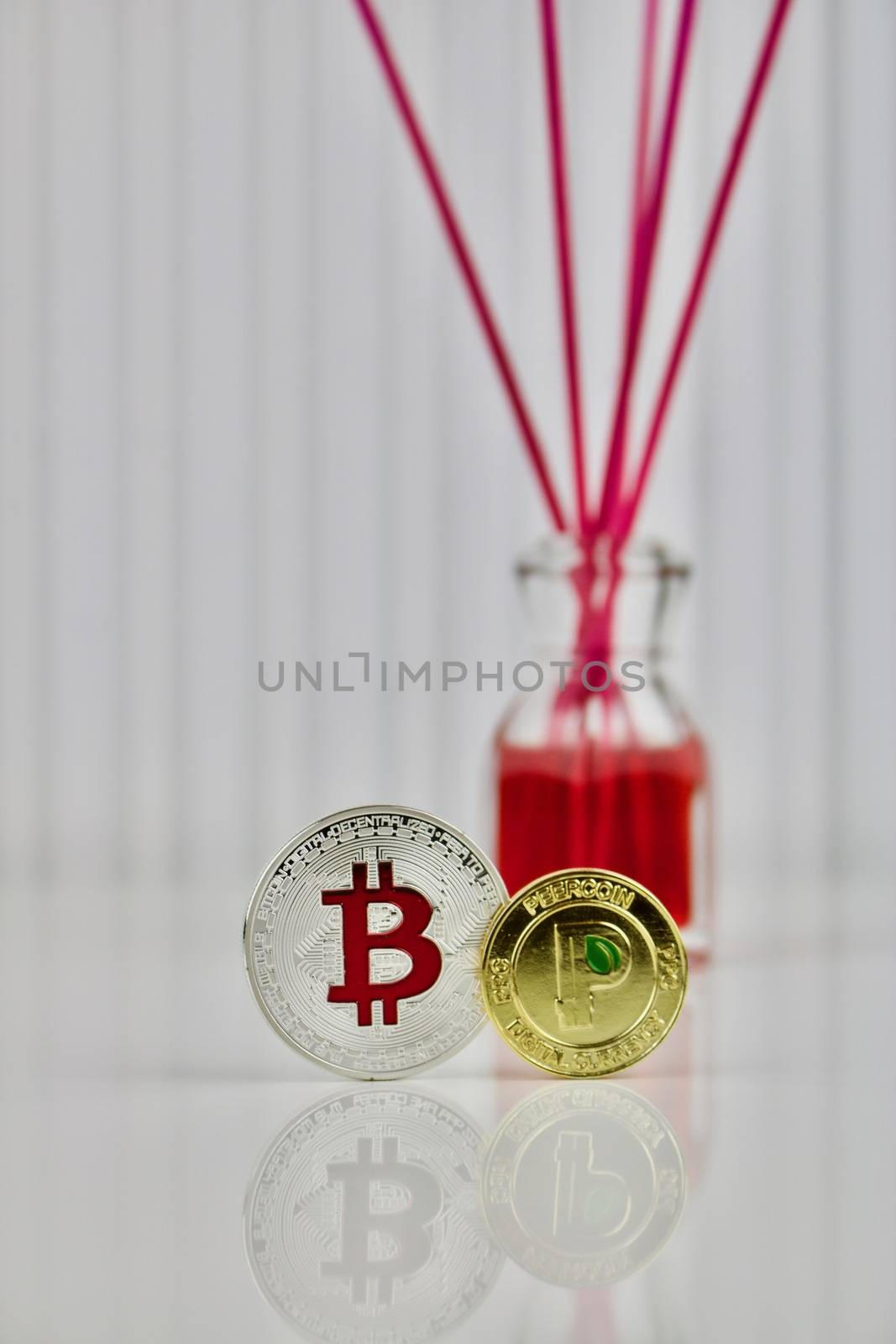 Digital currency physical silver bitcoin and gold peercoin near red bottle.