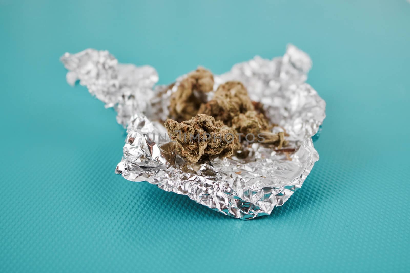 Green dry fresh marijuana in silver package on the green background.