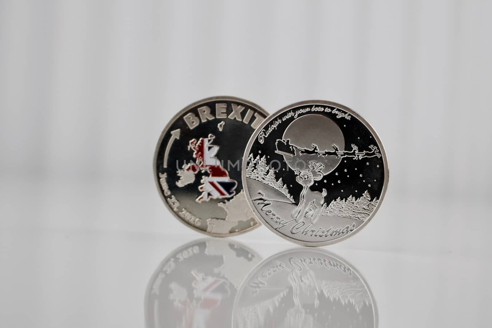 Silver brexit coin near silver christmas coin on the white table.