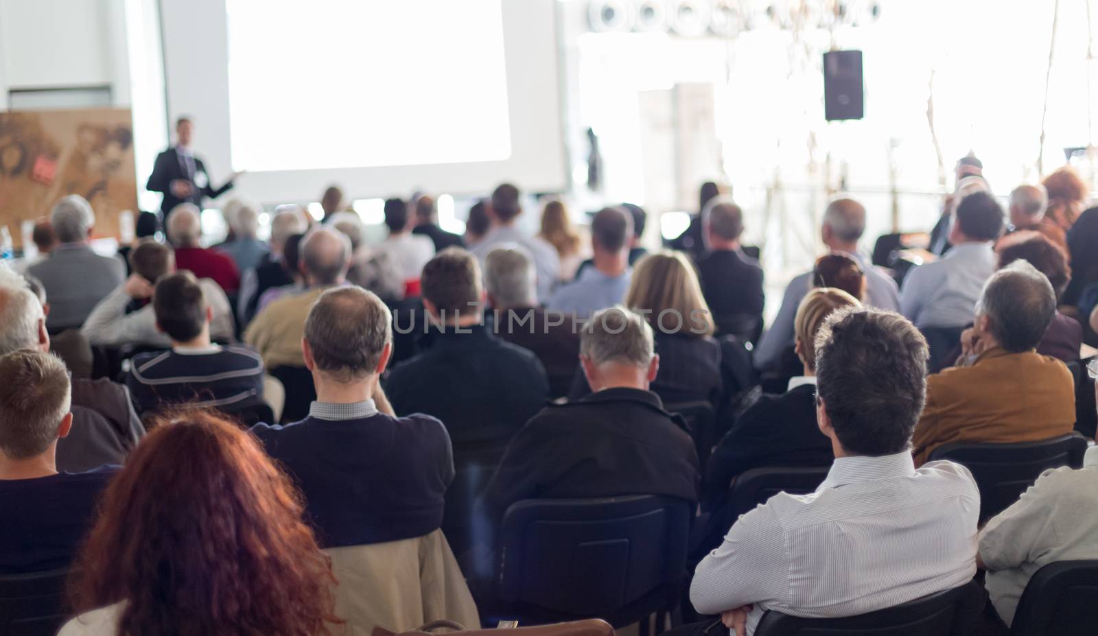 Speaker giving a talk in conference hall at business event. Audience at the conference hall. Business and Entrepreneurship concept. Focus on unrecognizable man in the audience.